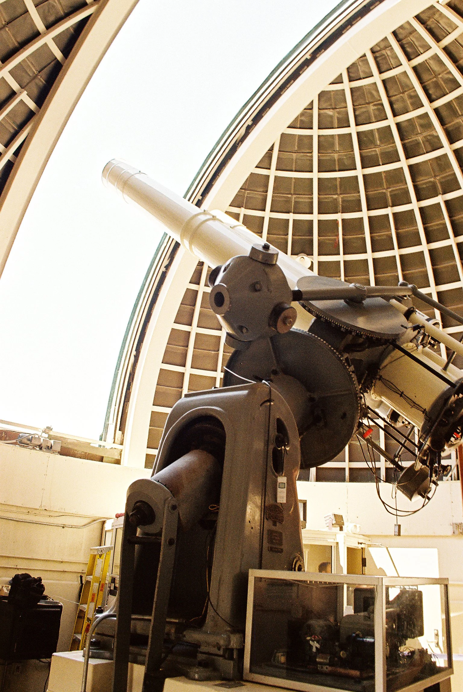 A large telescope mounted inside an observatory with a domed roof, viewed from below with equipment and supplies around.