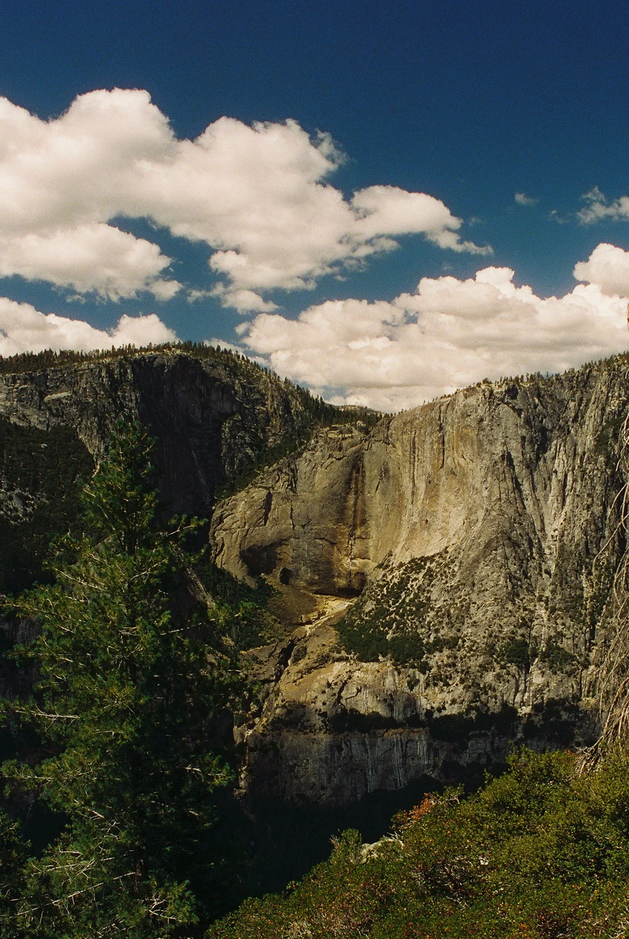 A scenic view of a mountain range with rocky cliffs and green trees under a partly cloudy sky.
