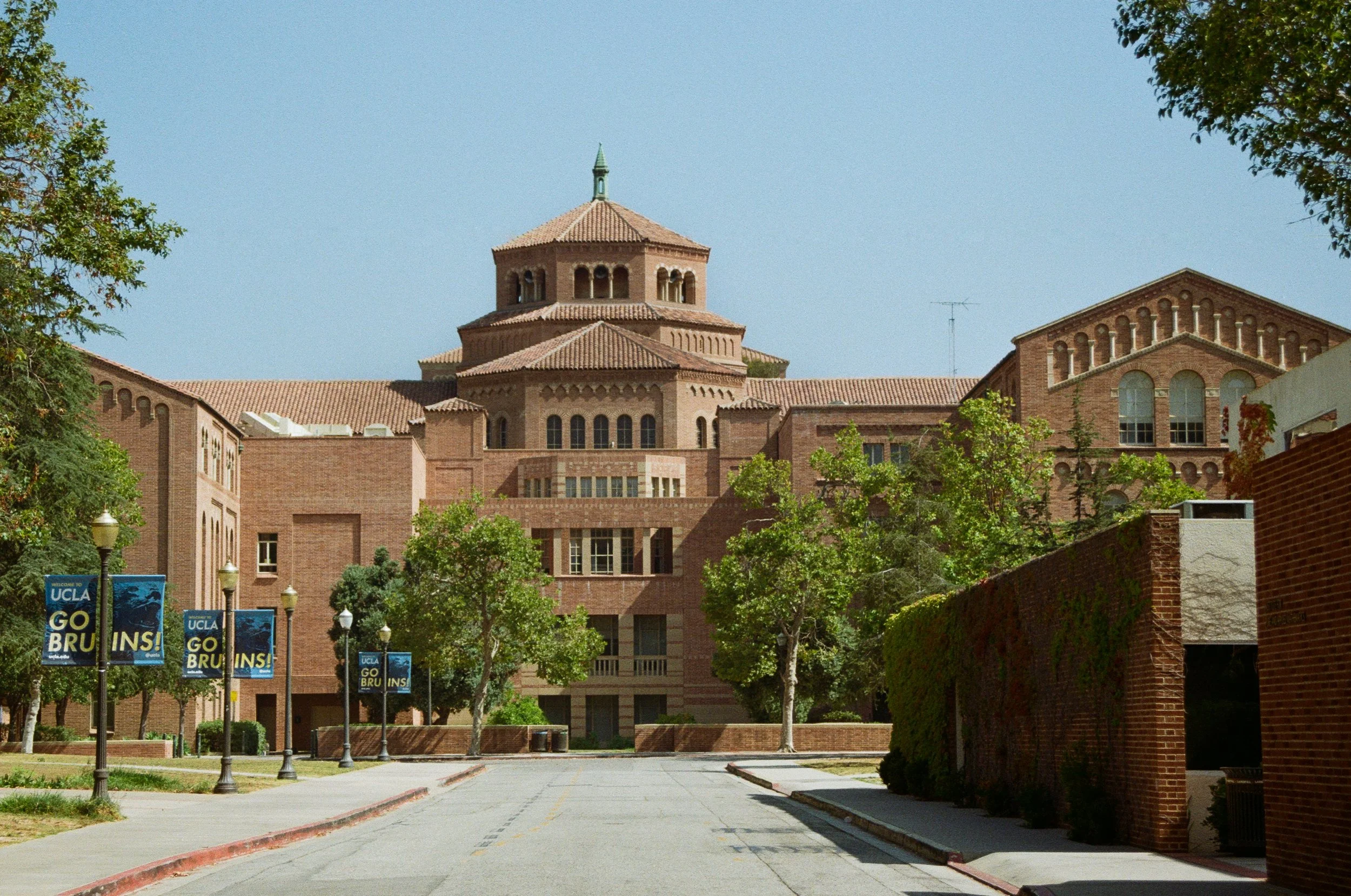 View of a university campus building with UCLA banners, trees, and a clear blue sky.