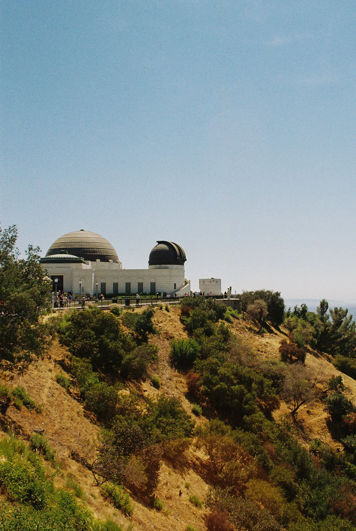 The Griffith Observatory situated on a hilltop overlooking Los Angeles, California, with a clear blue sky and surrounding greenery.