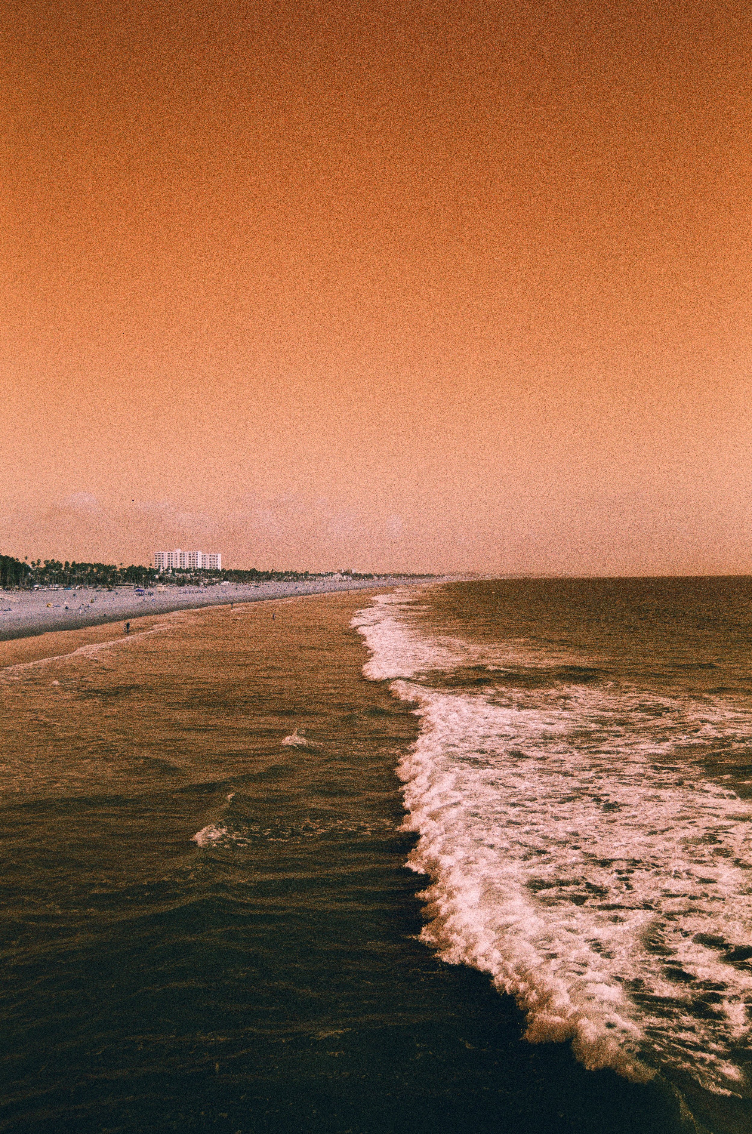 A beach scene at sunset with a rainbow in the sky and buildings in the distance.