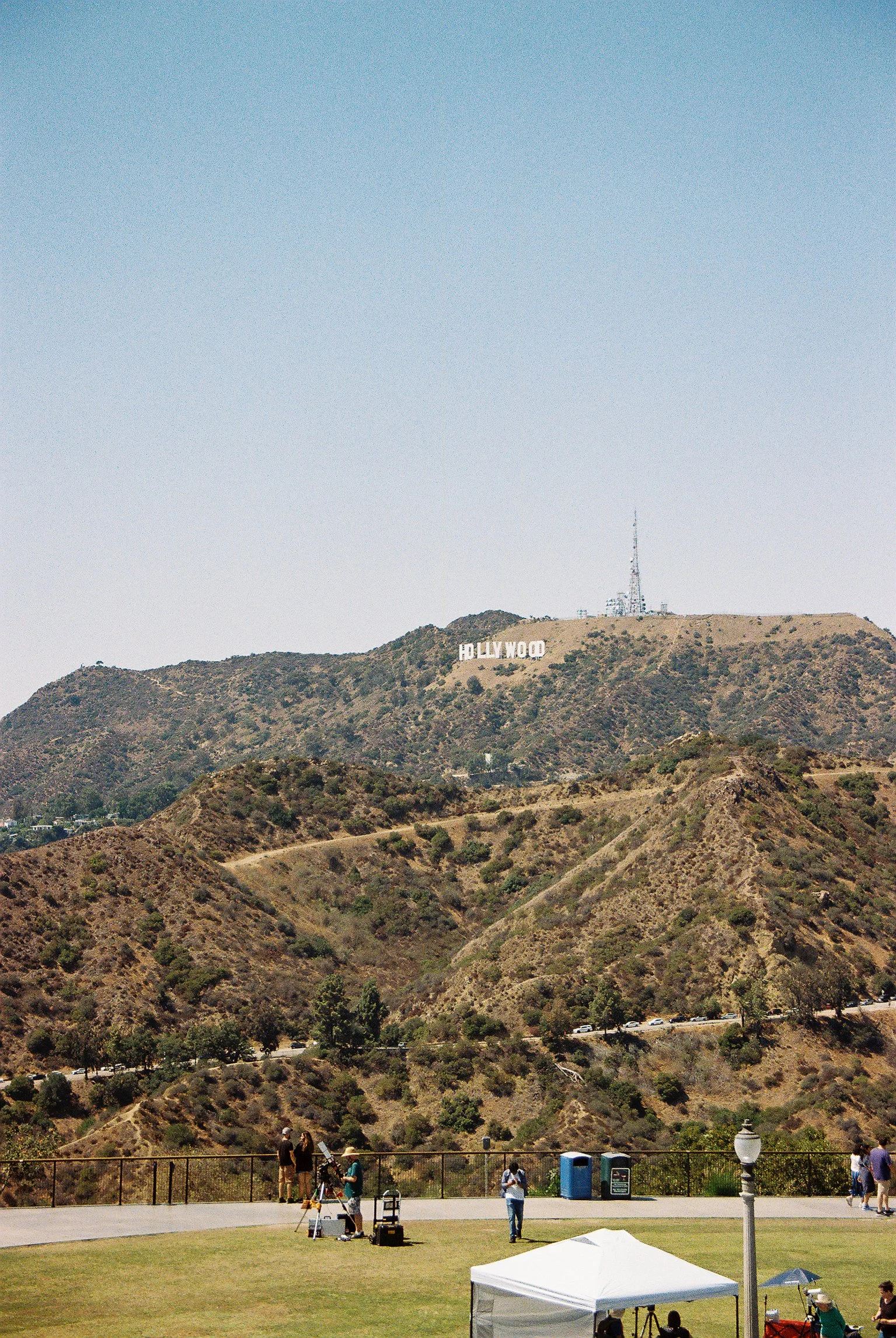 Hilly landscape with the Hollywood sign on a hill and a communication tower, with people and equipment in the foreground at a park.