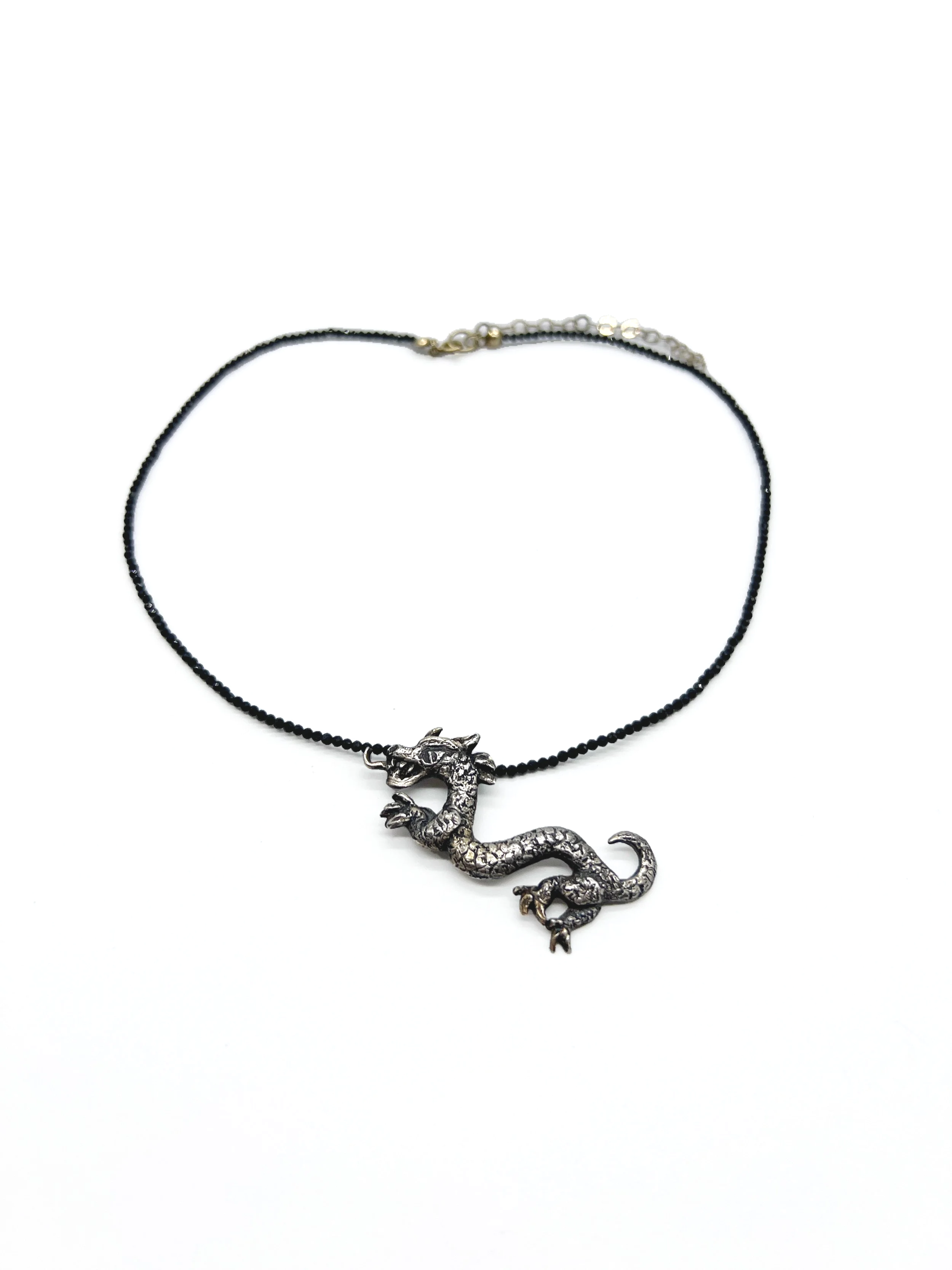 A necklace with a silver dragon pendant on a black cord.