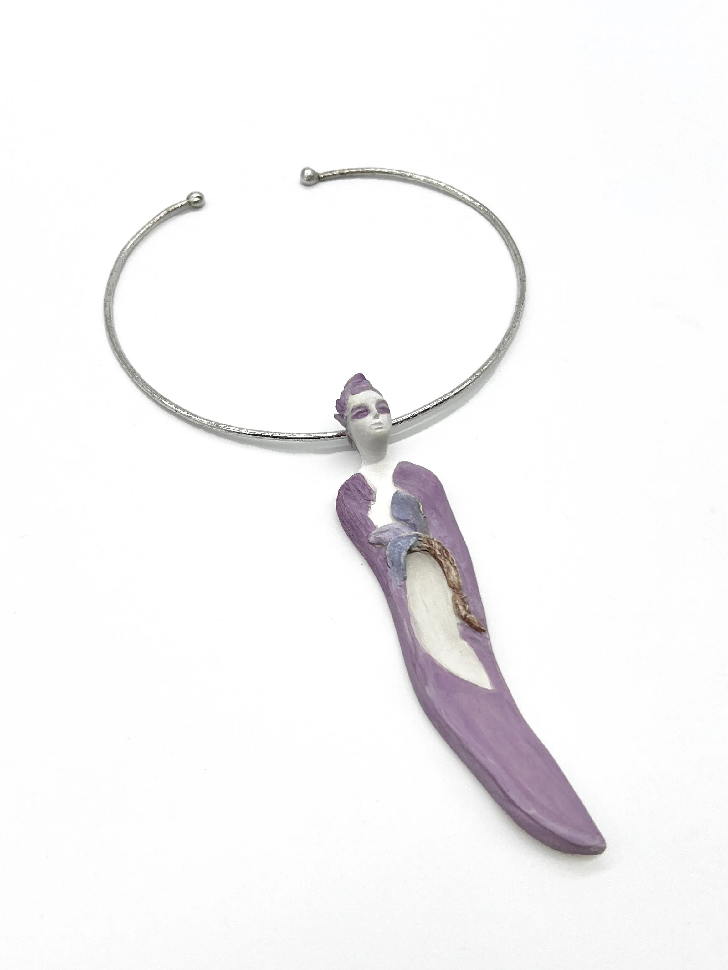 A jewelry bracelet with a small figurine of a woman attached to it, painted in purple and white with a painted face and hair, and a painted dress.