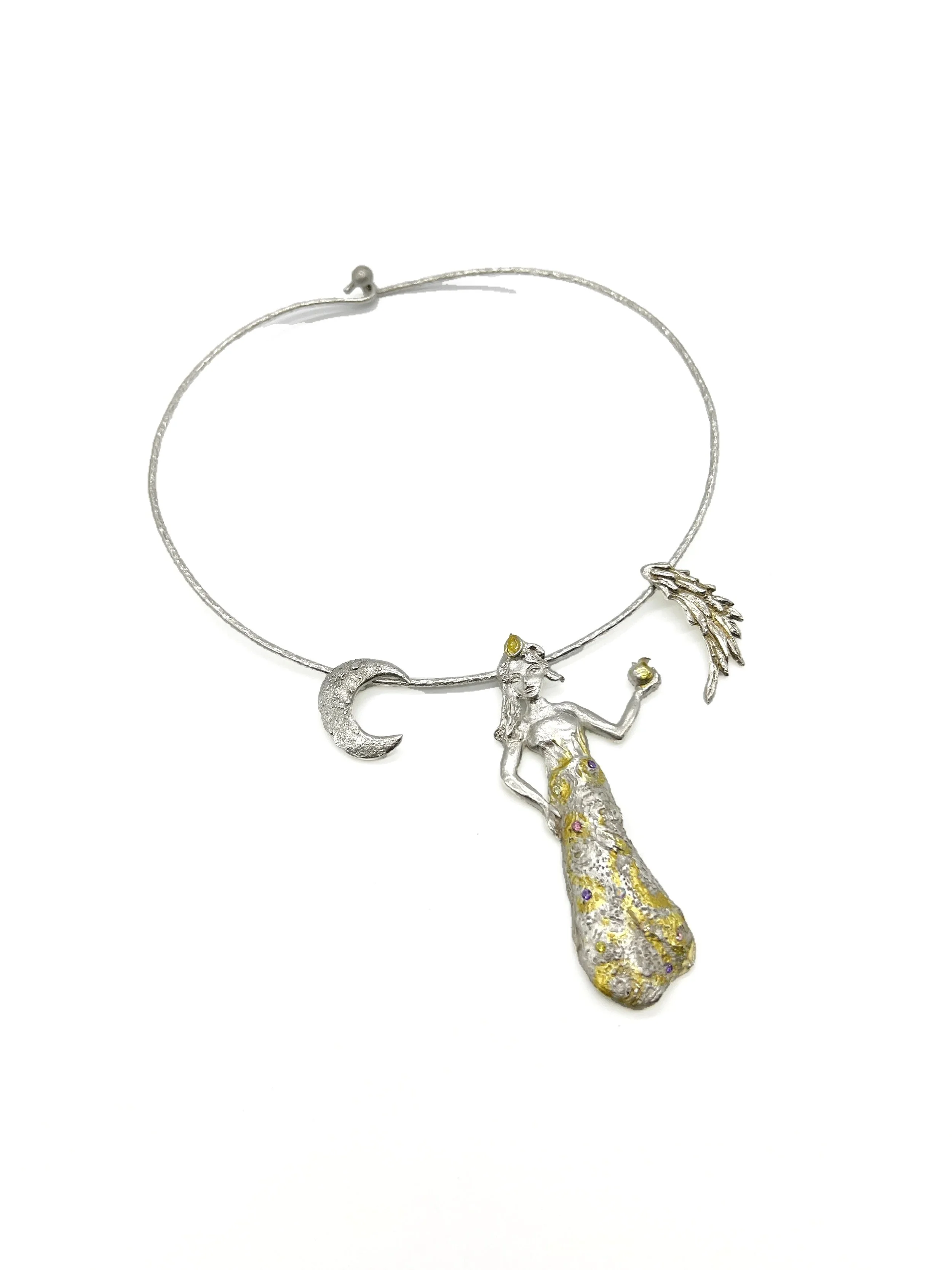 A decorative necklace featuring a detailed figure of a mermaid with a silver top, gold and purple embellishments on the tail, holding a yellow gemstone, with a moon and a feather charm.