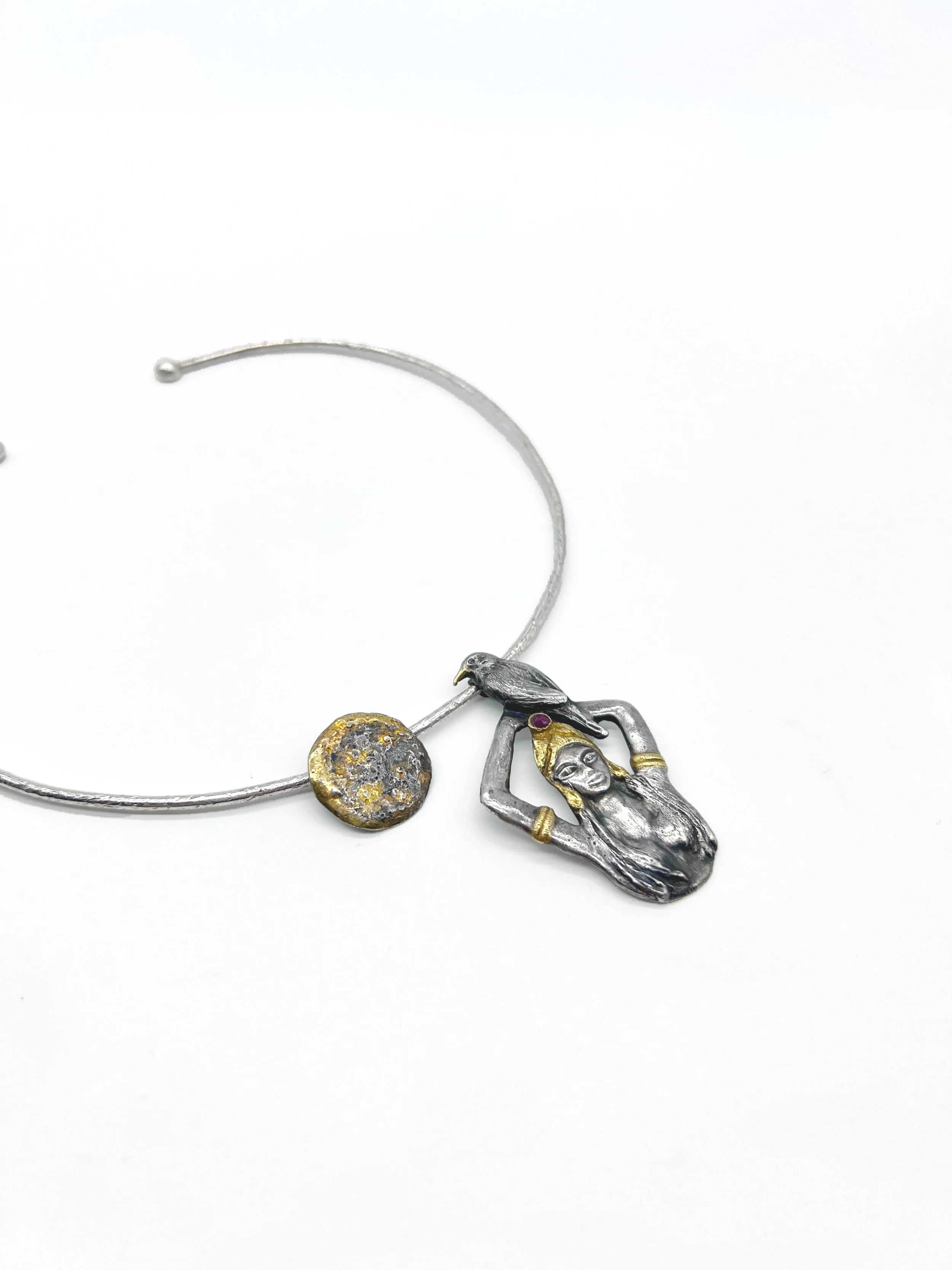 Silver necklace with a pendant featuring a woman lying down with hands behind her head, gold accents, a purple gemstone, and a textured circular charm, against a white background.