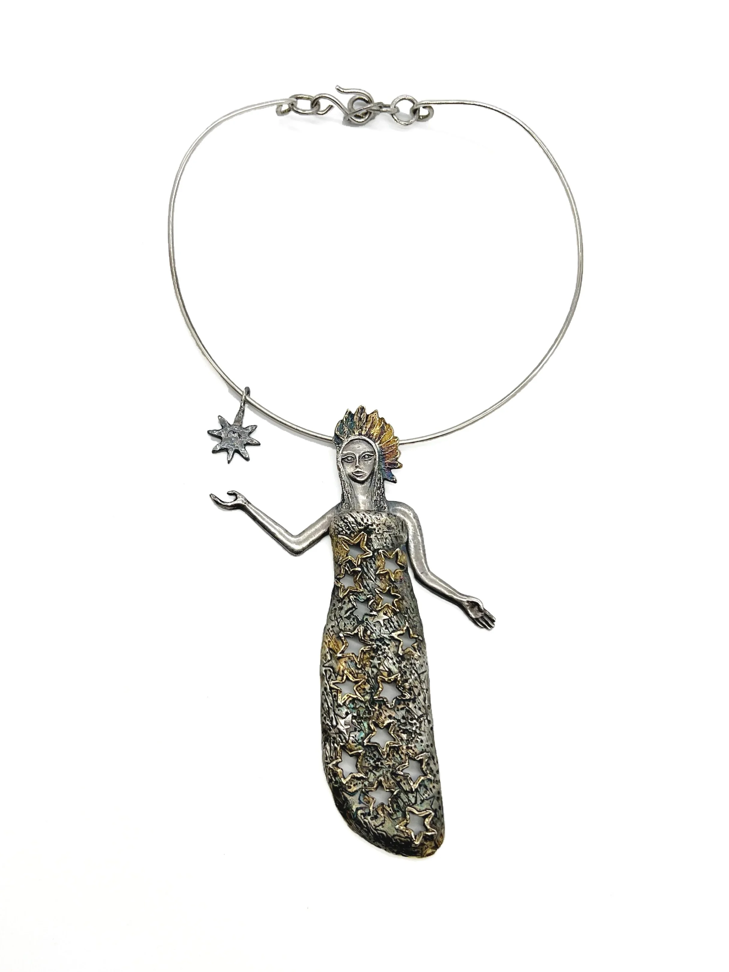 A silver necklace with a pendant shaped like a woman with long hair, a feathered headdress, and a dress made of cut-out stars. The necklace has a star charm and a small moon charm.