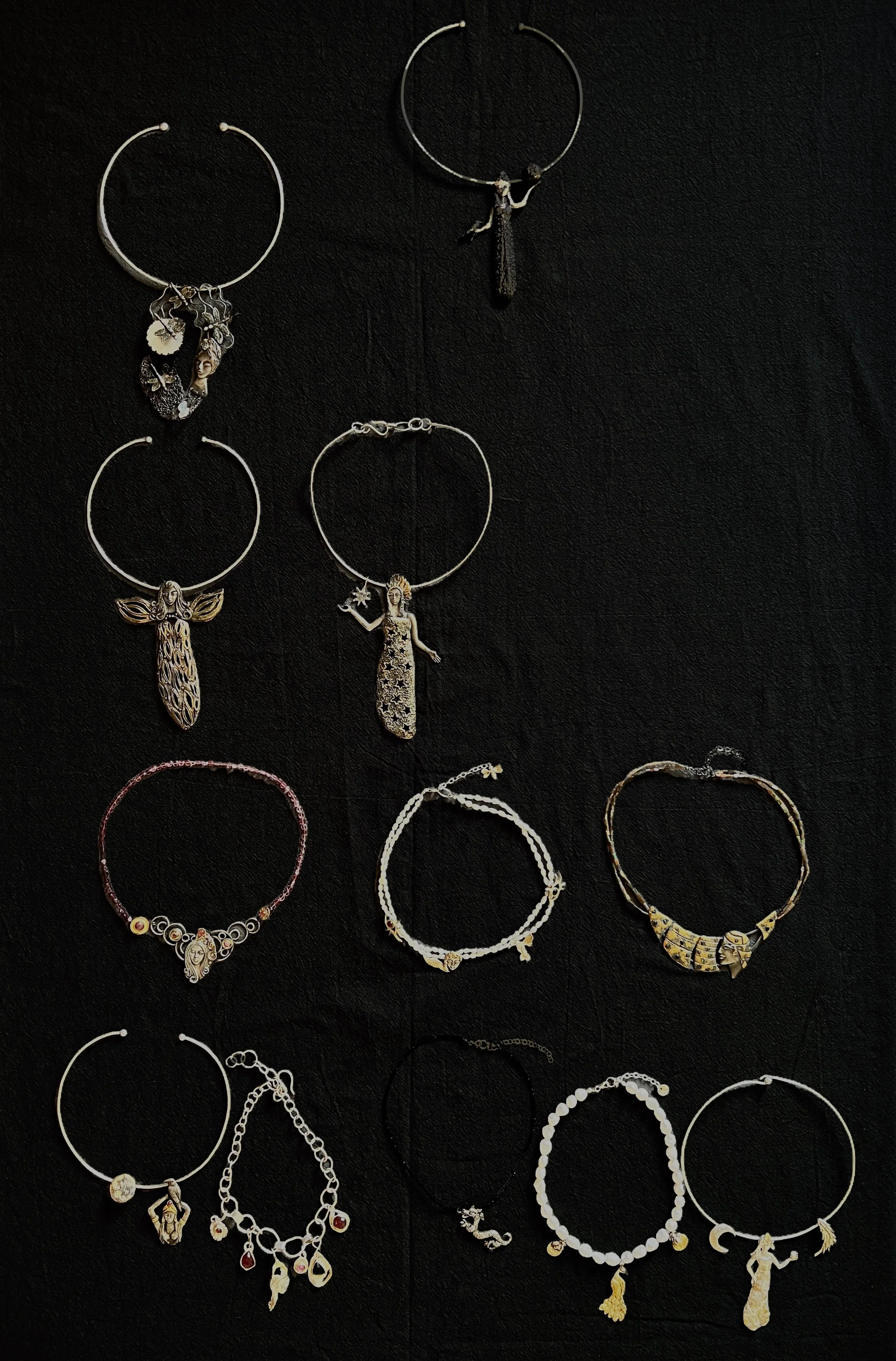 Collection of various necklaces on a black background, including silver, gold, and beaded styles, with charms such as princesses, fairy, and other figures.