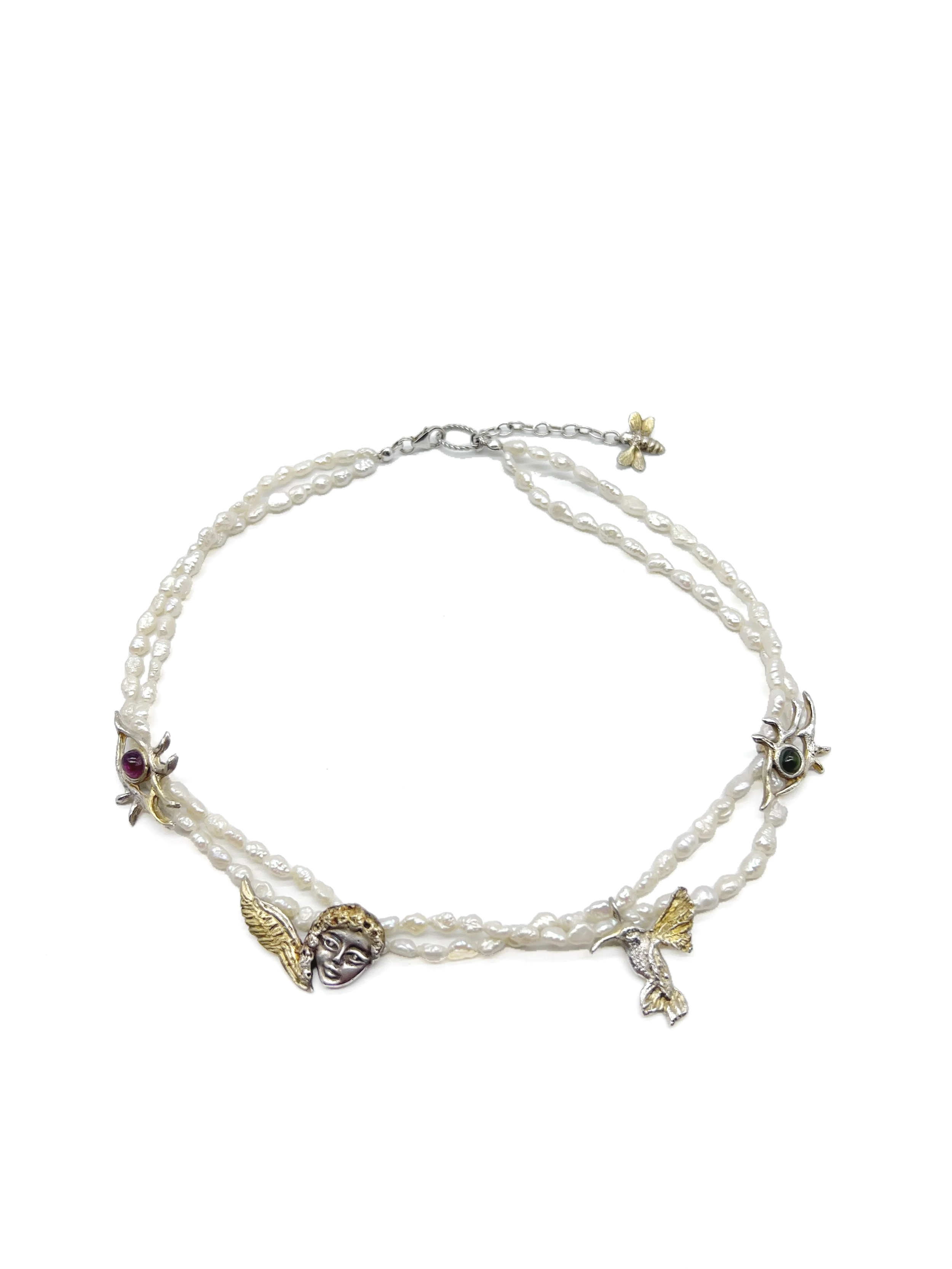 A multi-strand pearl necklace with decorative gold and silver charms, including faces, wings, and animals, arranged on a white background.