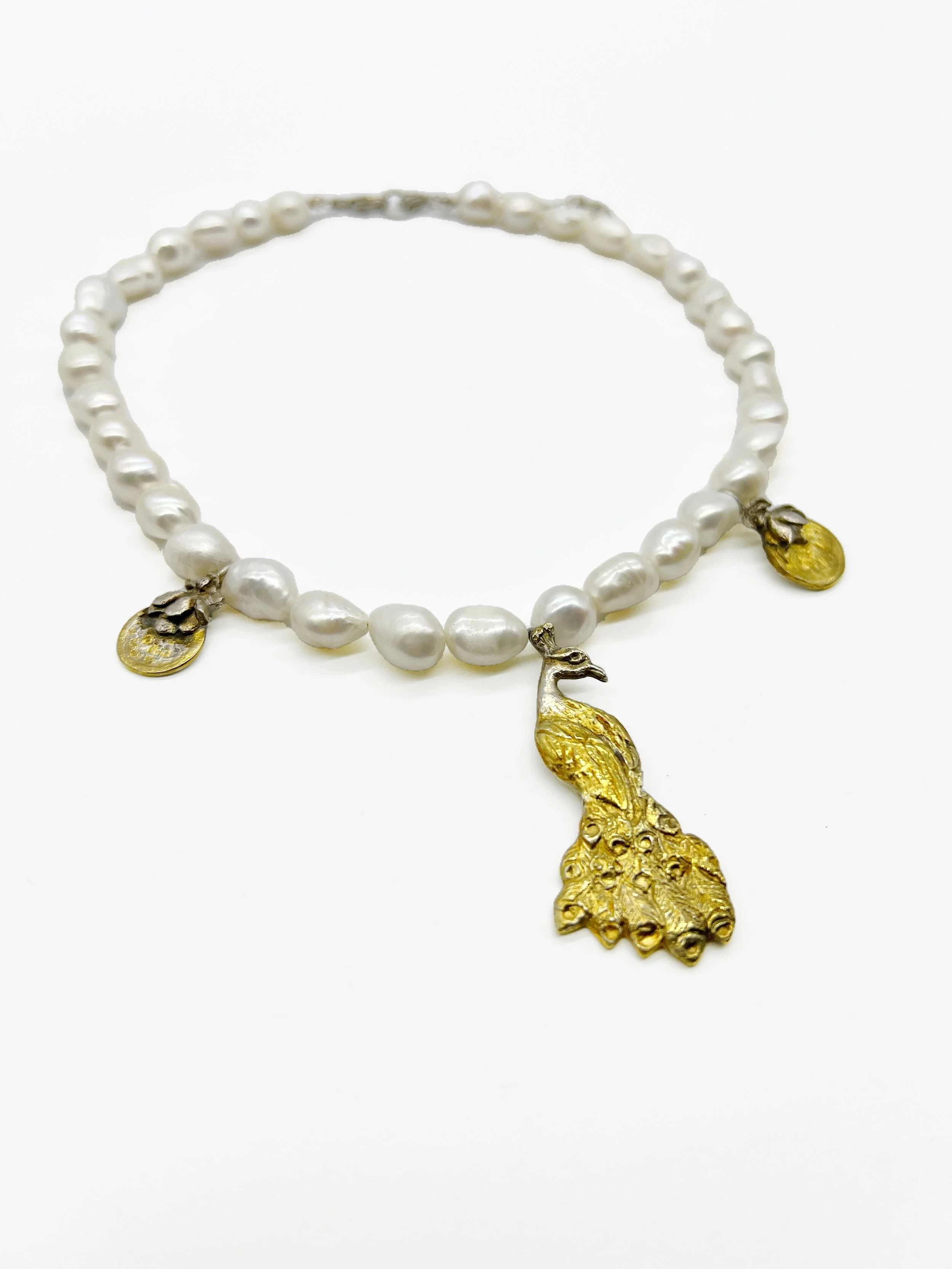 A pearl necklace with gold-colored pendant and charms resting on a white background.