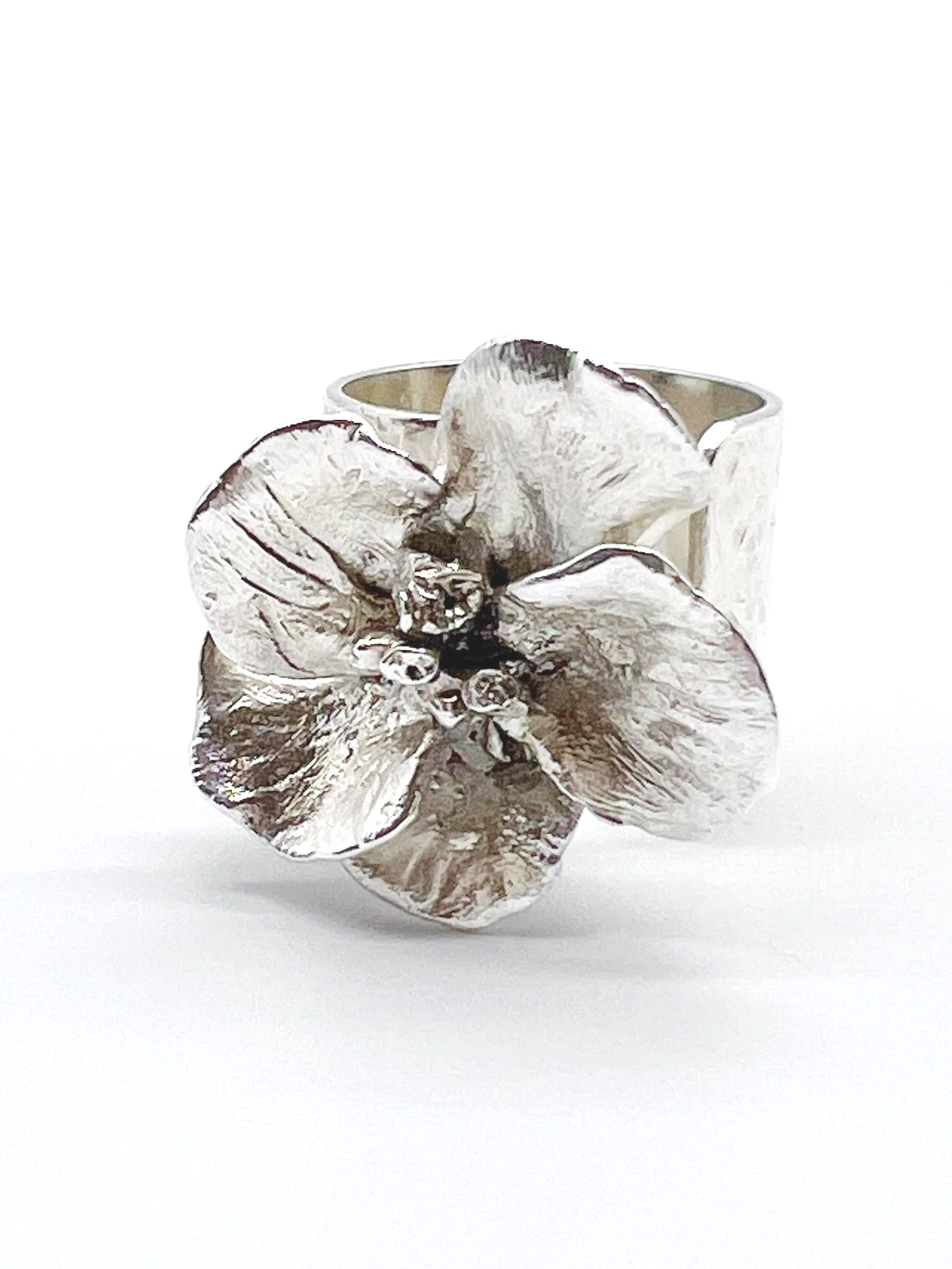 Silver flower-shaped ring with detailed petals and small central accents, displayed against a plain white background.