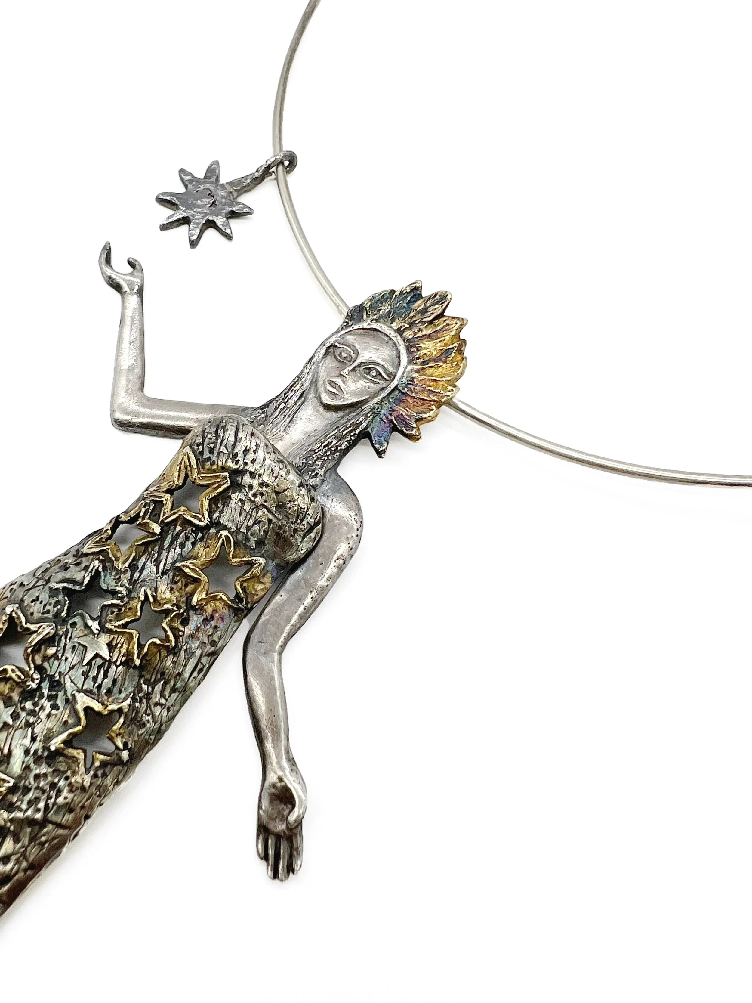 Silver and gold jewelry featuring a figure of a woman with a feathered headdress, with intricate star and moon designs surrounding her.