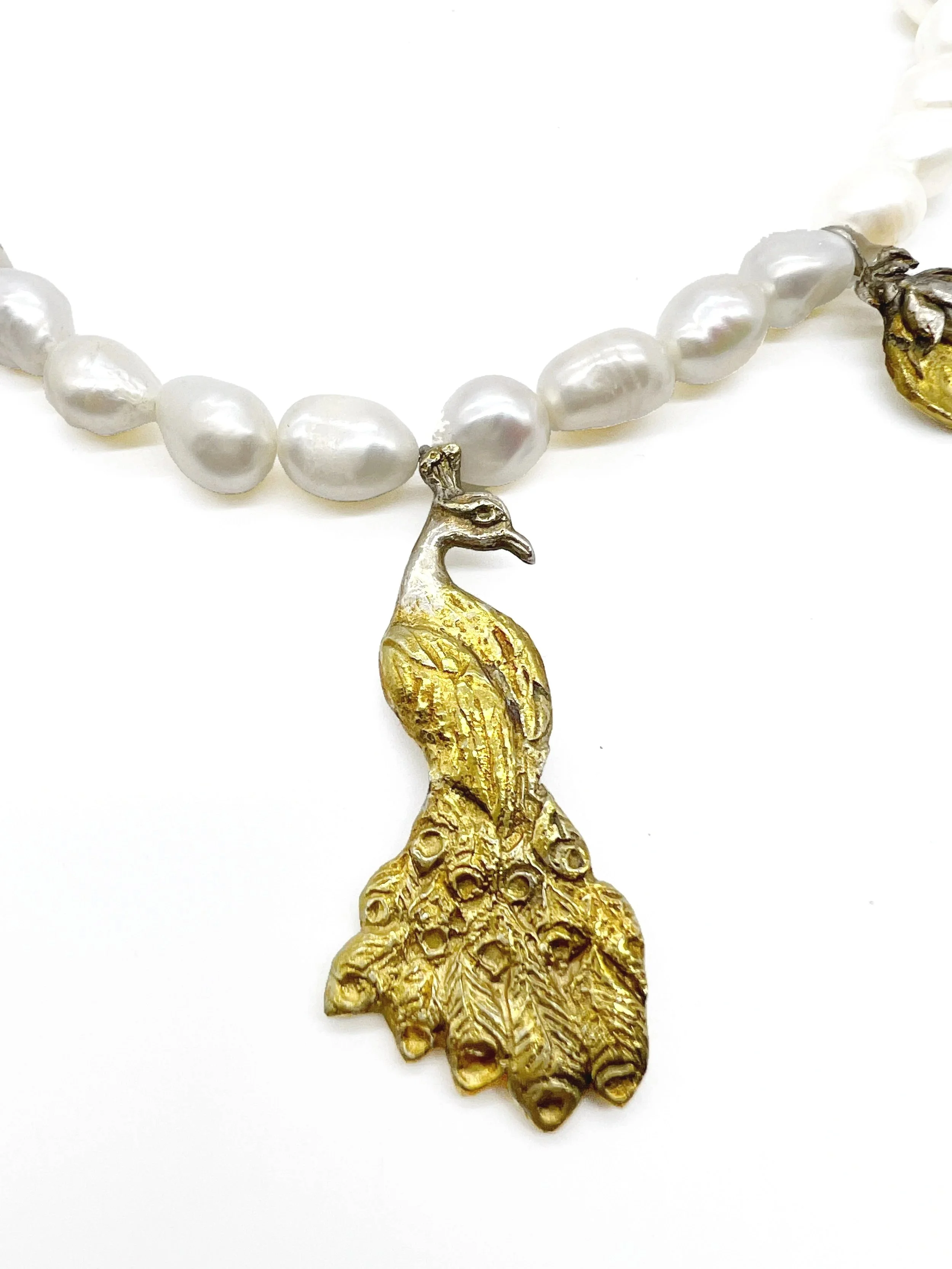 Close-up of a white pearl necklace with a gold peacock pendant.
