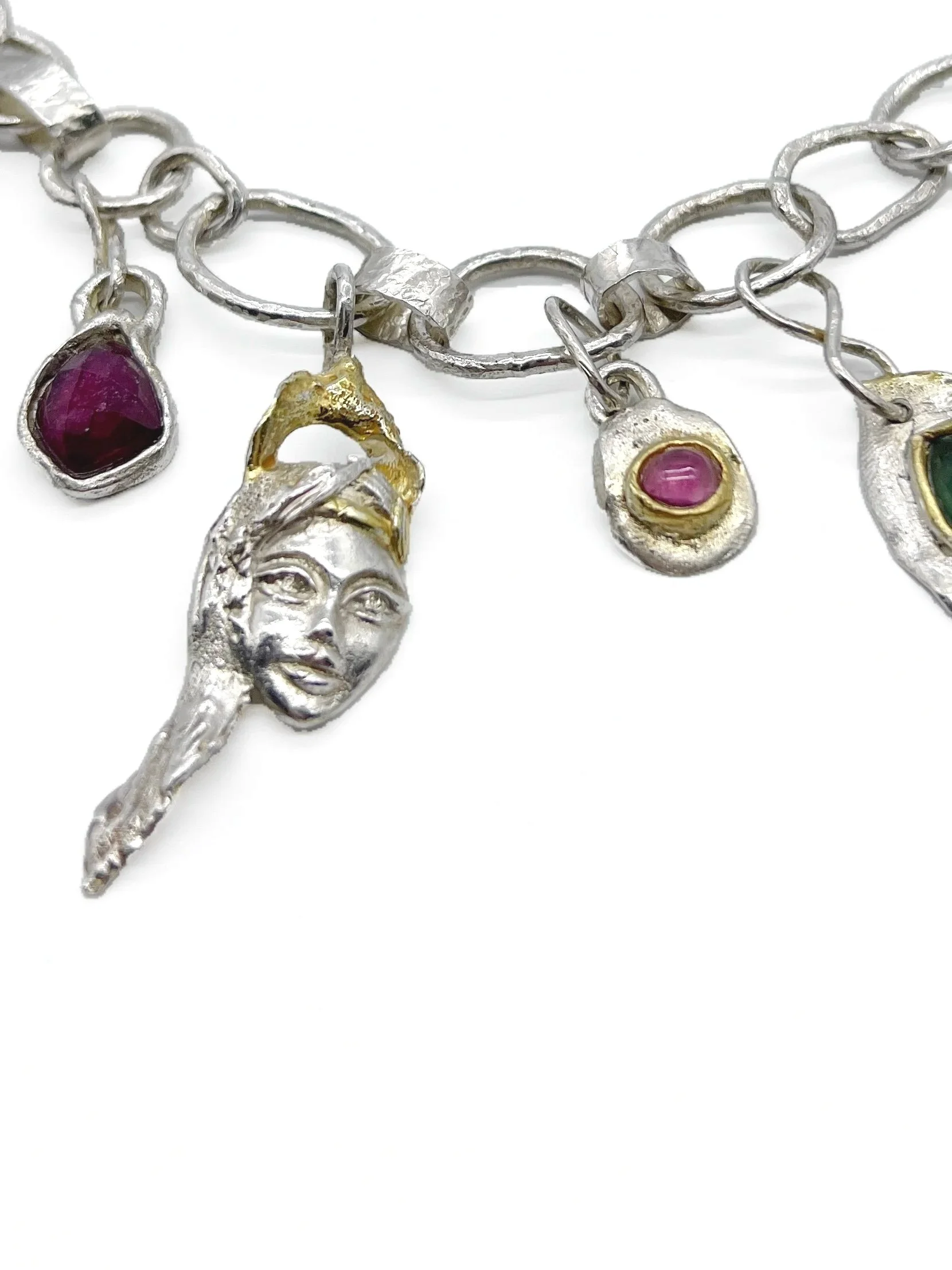 Close-up of a silver bracelet with charms, including a face, a red gemstone, and a gold accent, on a white background.