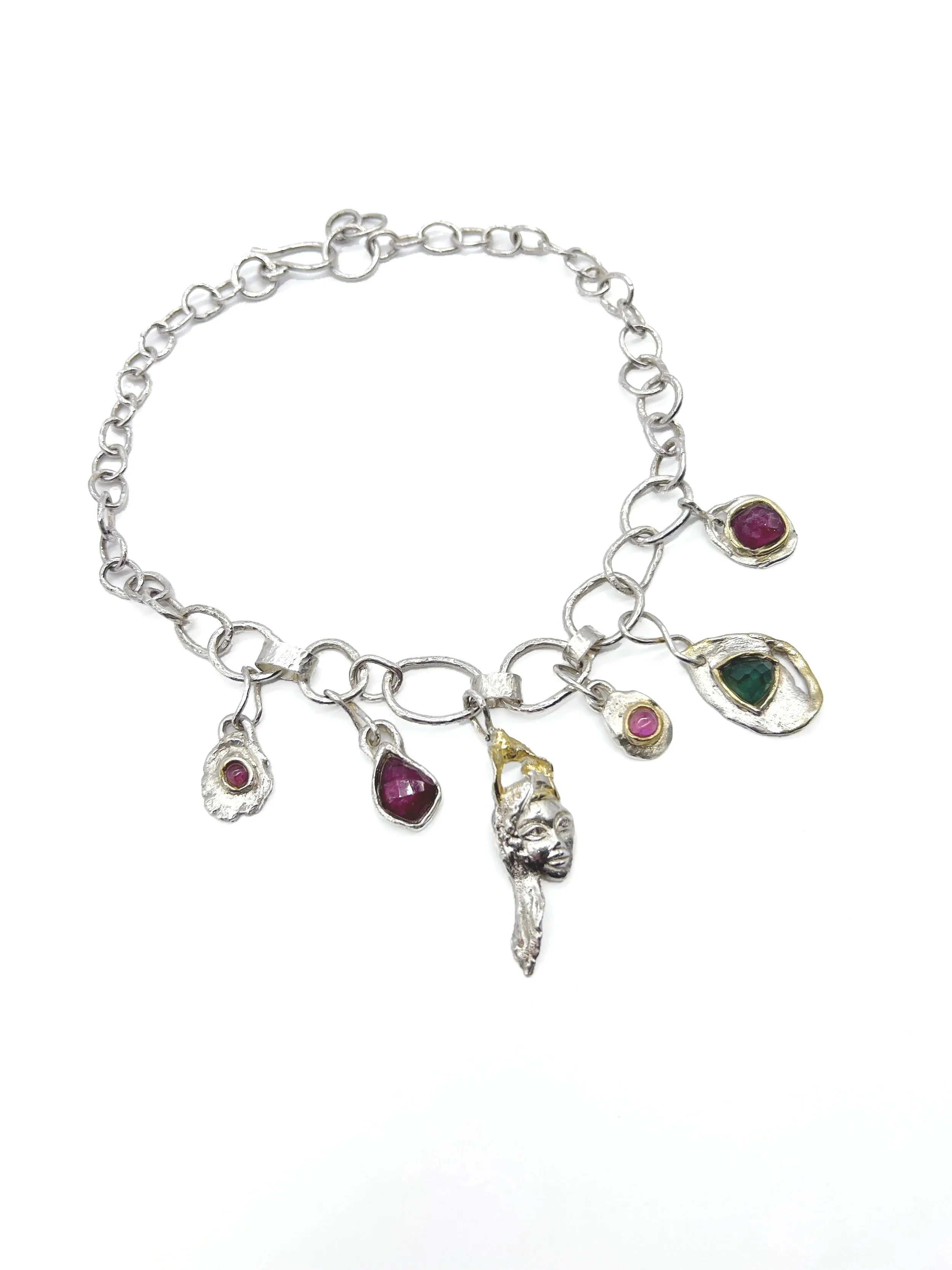 Silver charm necklace with colorful gemstone pendants, including a face and a hand, placed on a white background.