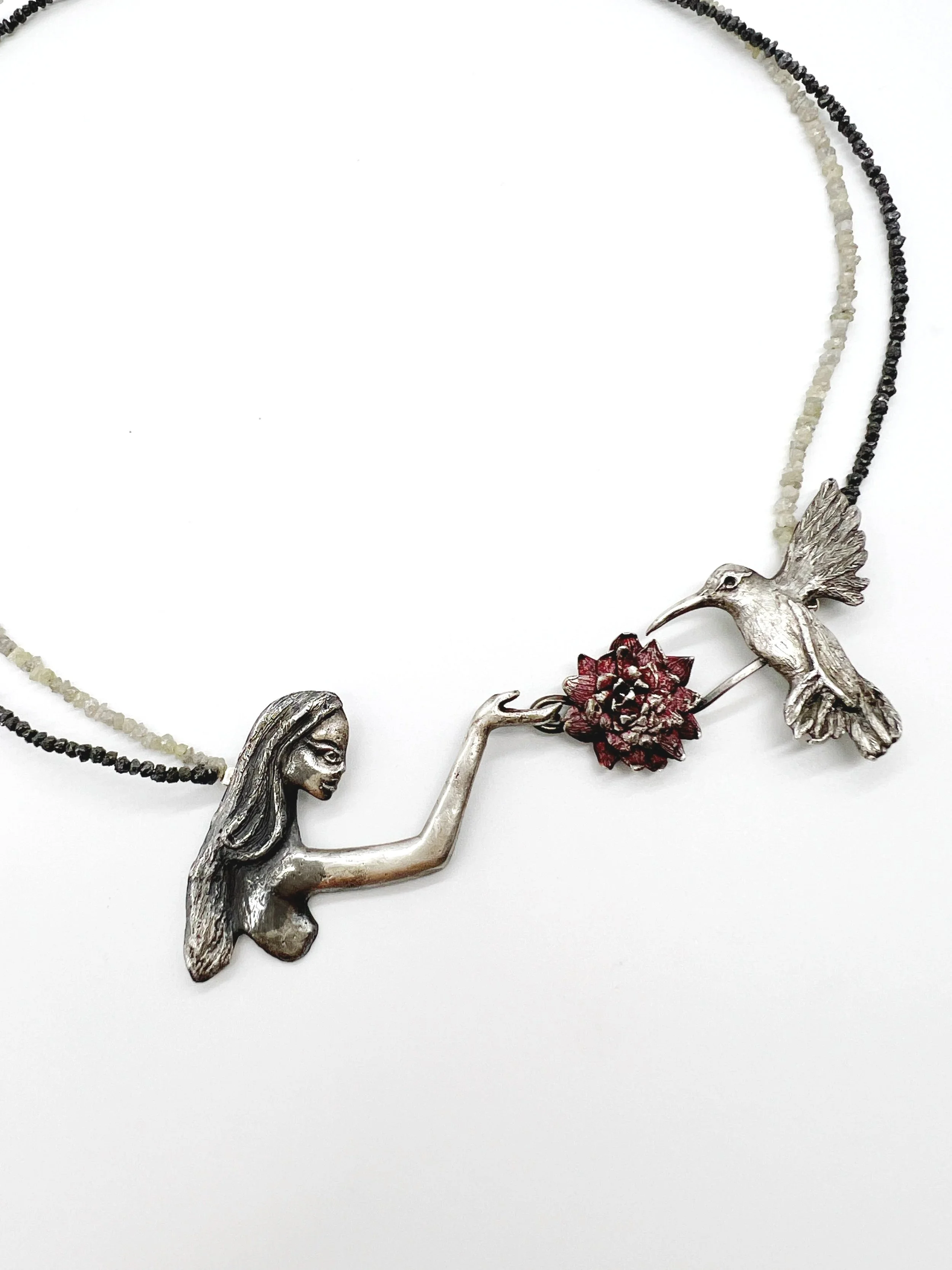 A necklace with a silver hummingbird pendant and a small red flower, with beads in black, white, and red colors.