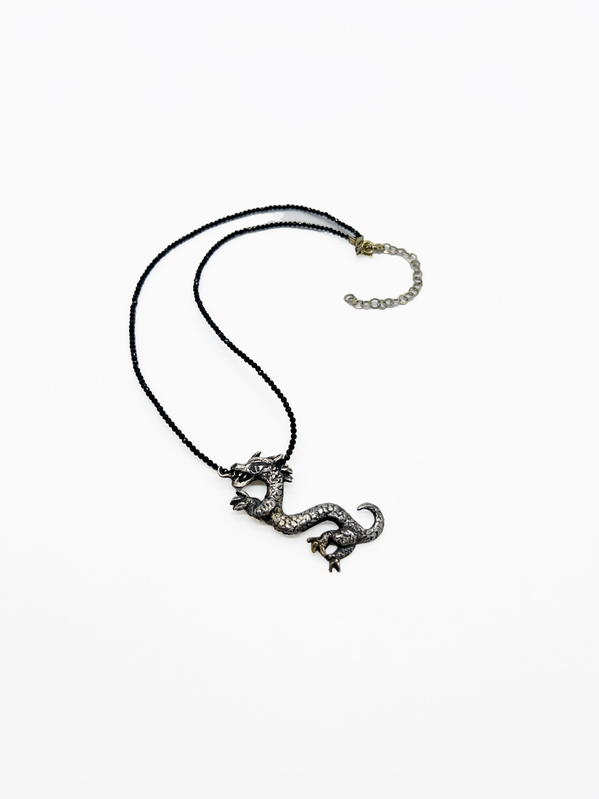 Silver dragon-shaped necklace with a black beaded chain on a white background