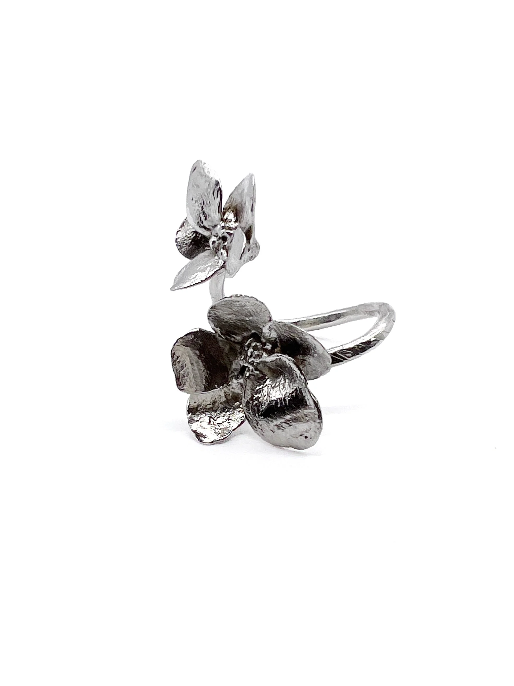 A silver-colored ring with a flower design and an wing detail, made of shiny metal, is displayed against a white background.