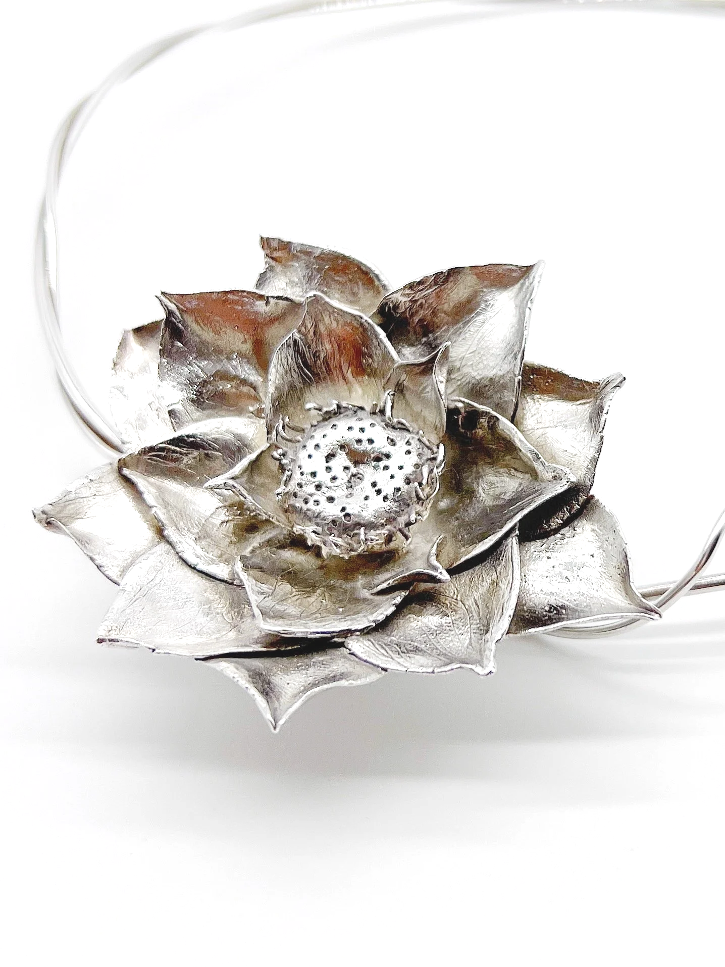 A decorative silver-colored metal flower brooch with layered petals and a circular center, displayed against a white background.