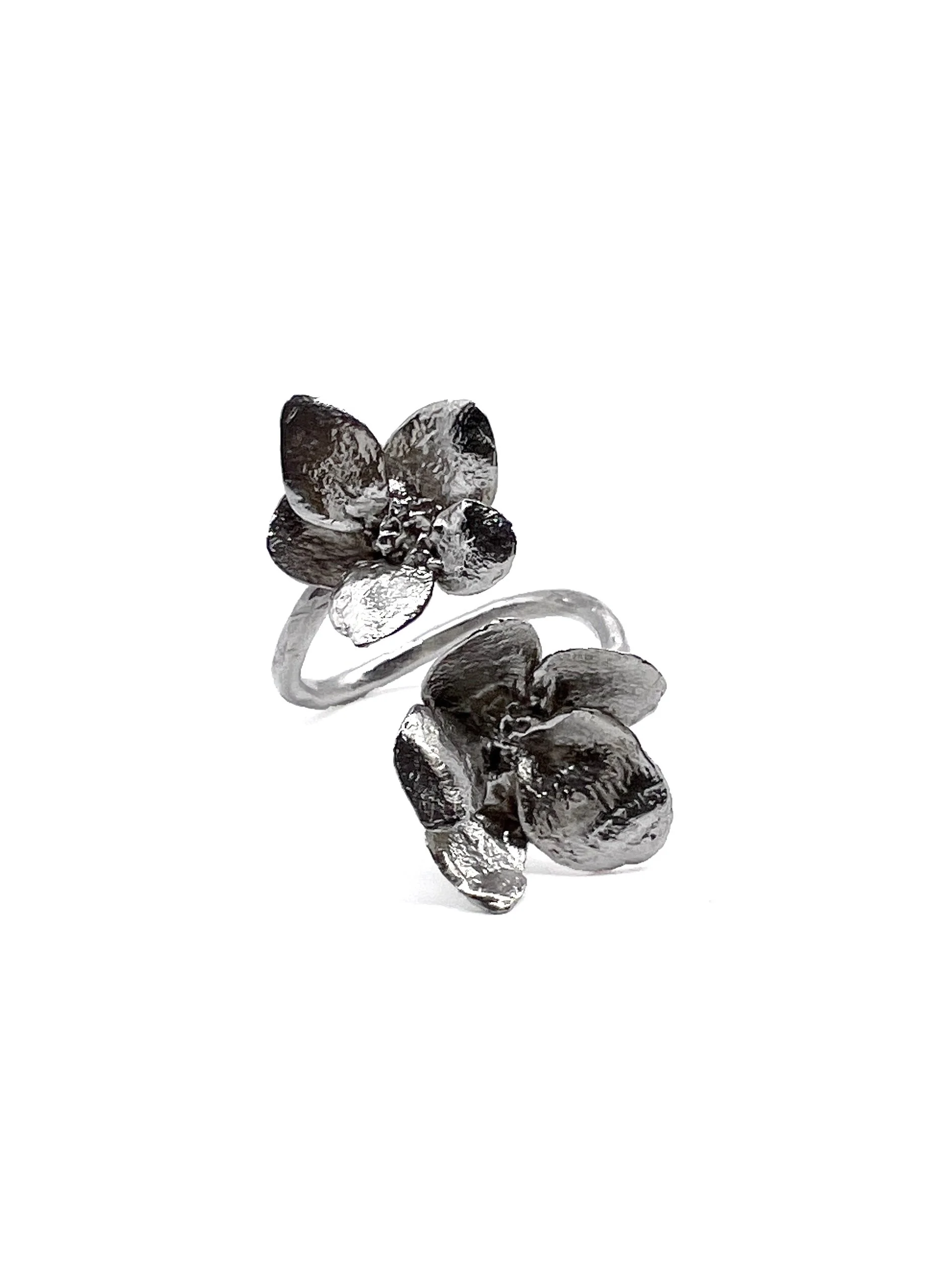 Silver ring with a flower design and dark stones, placed on a reflective surface.