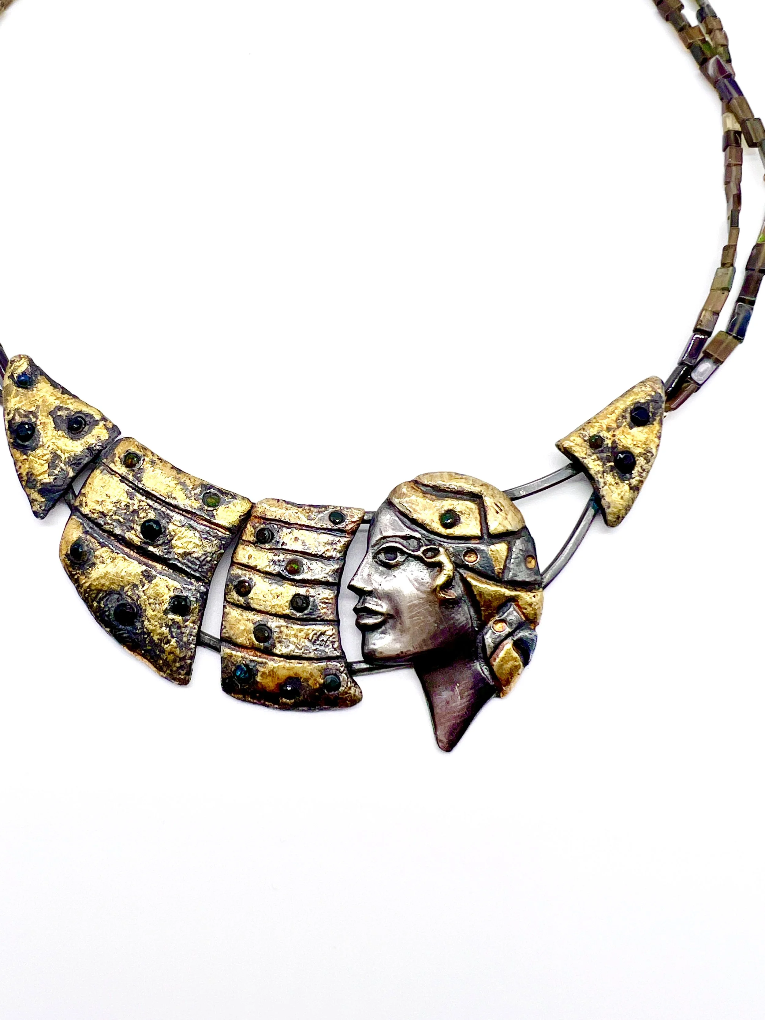 A necklace with gold, silver, and multicolored stones in various geometric and human face shapes.