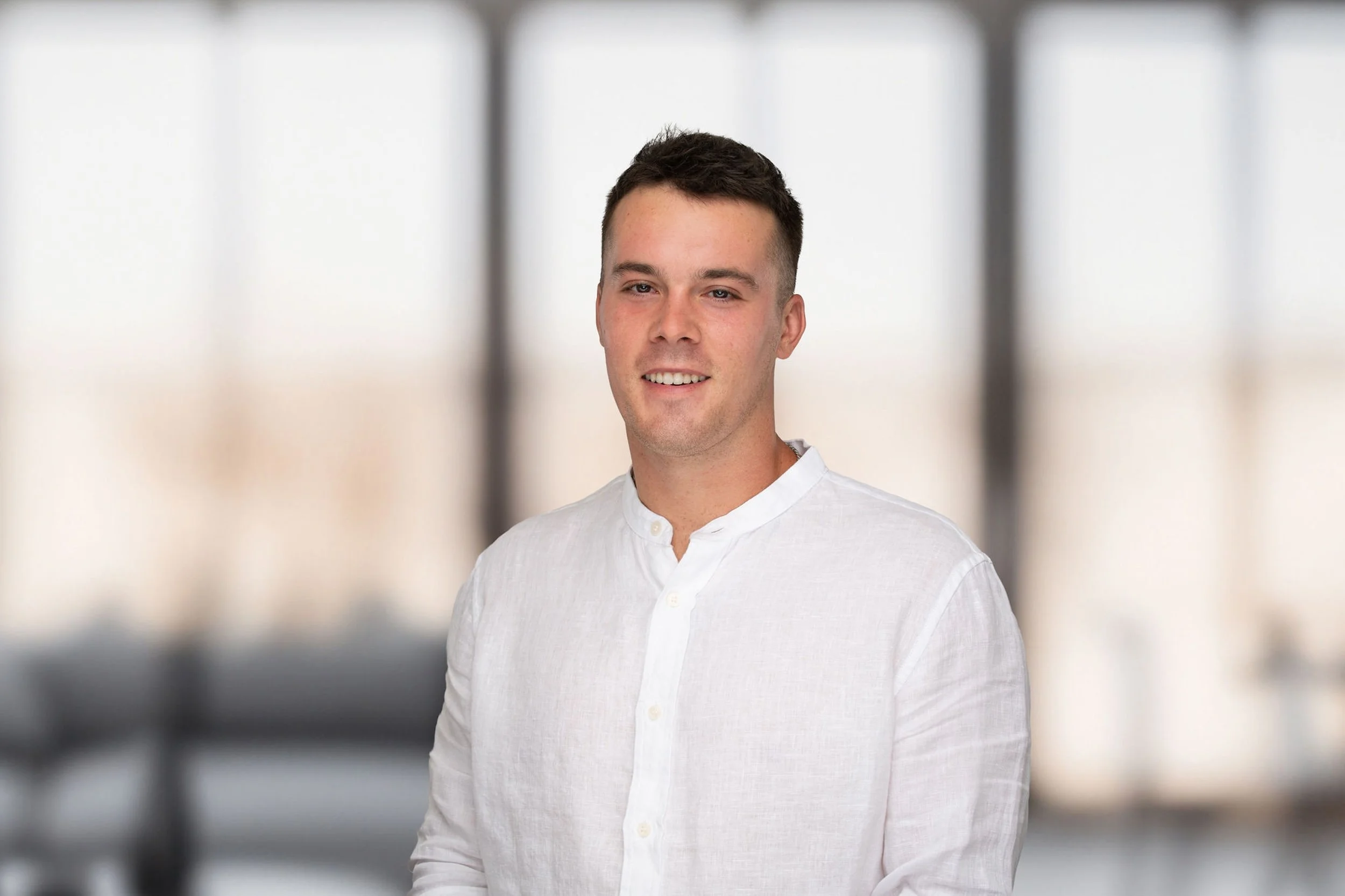 Grayson McGraw in a white shirt, standing beside large windows.