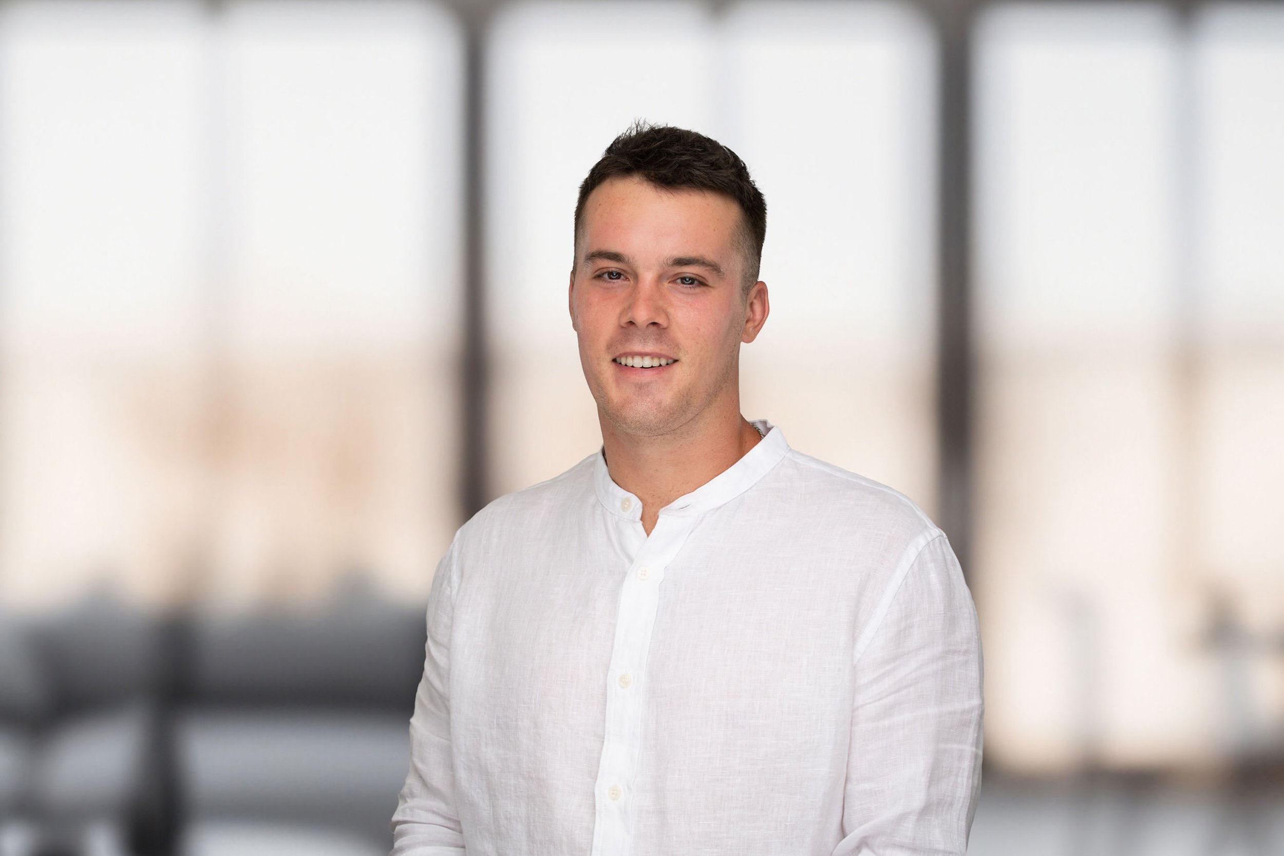 Grayson McGraw in a white shirt, standing beside large windows.