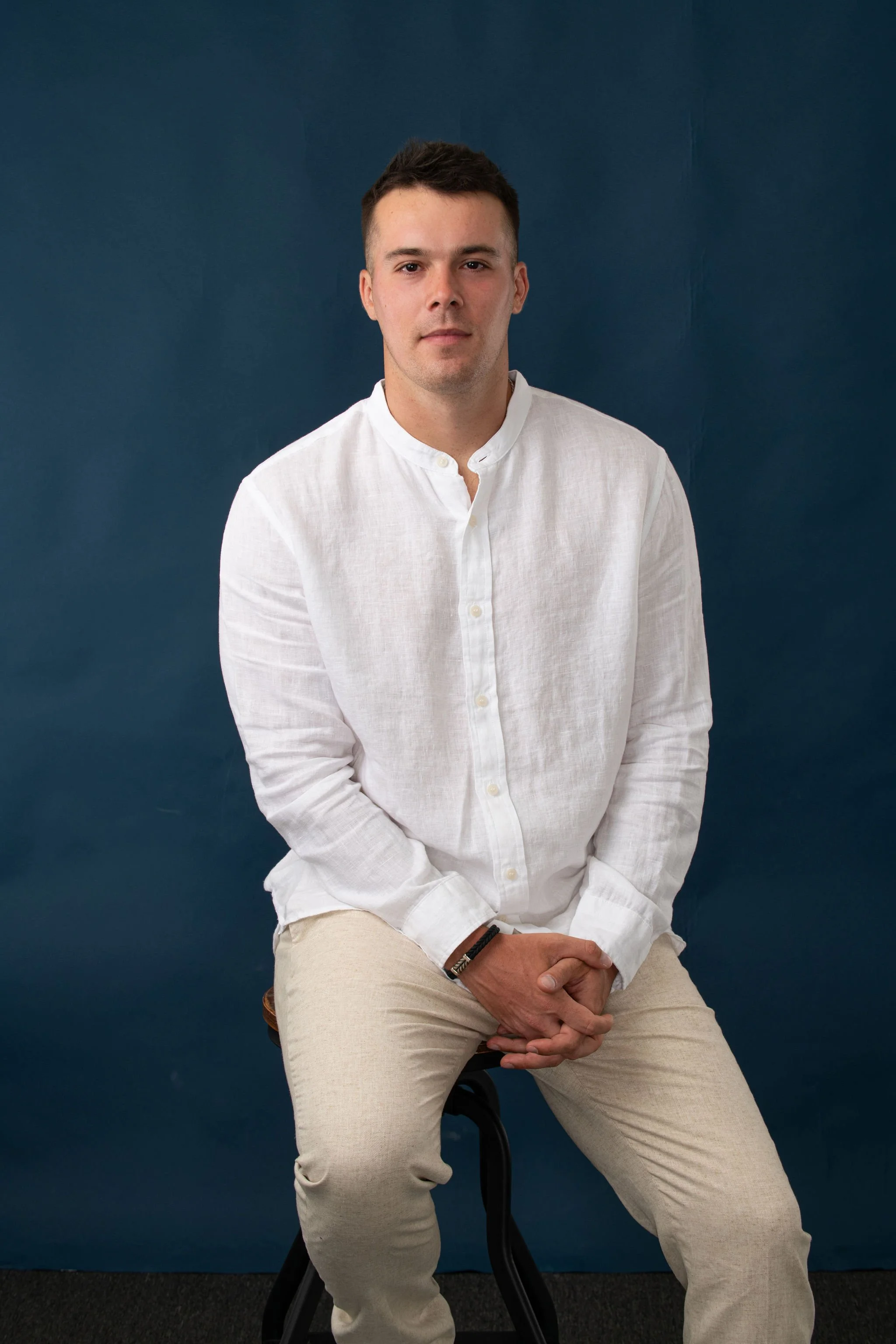 Grayson McGraw, men’s coach, seated in a white shirt against a dark blue background.