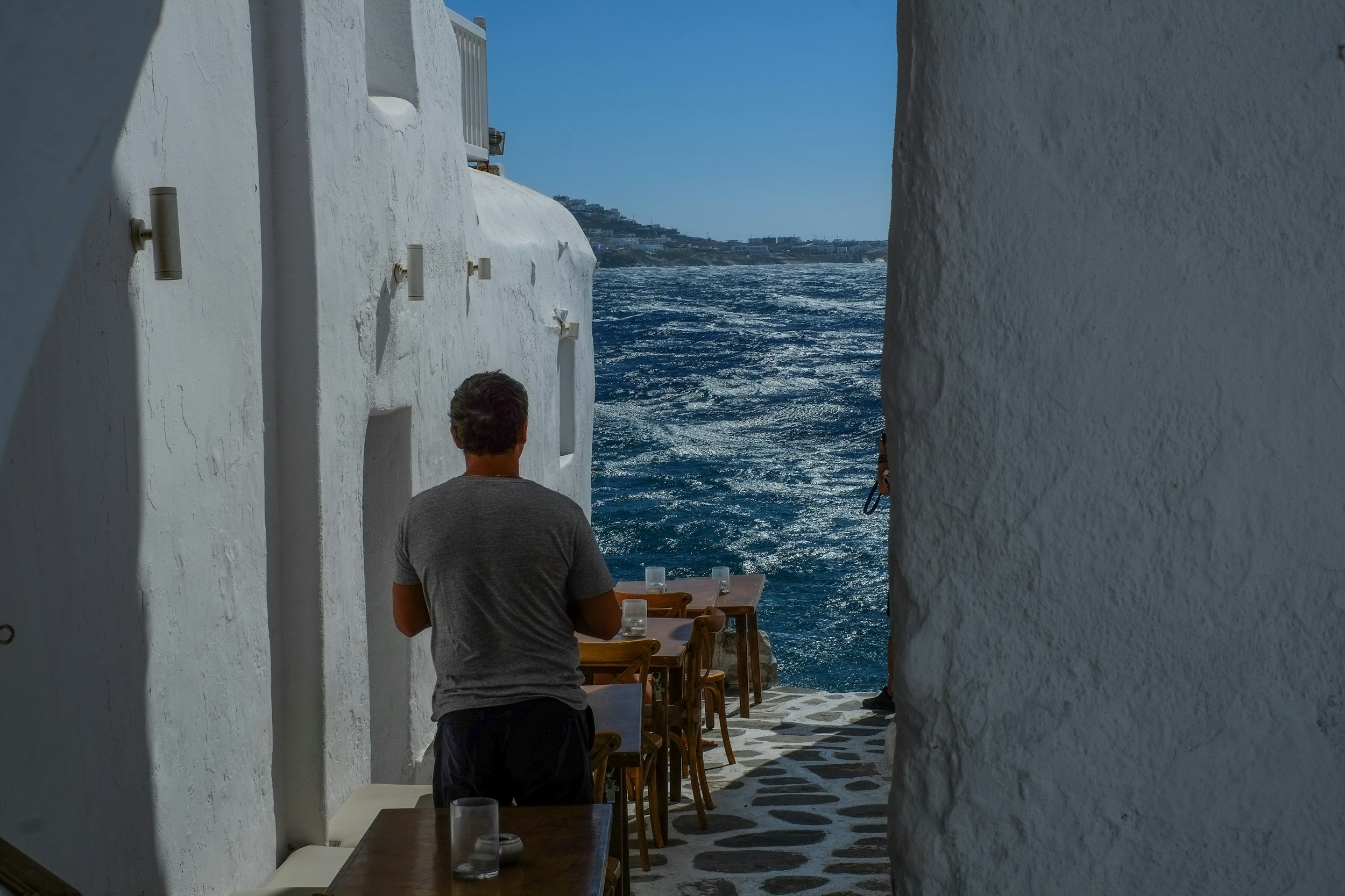 Person walking between whitewashed buildings toward the sea.