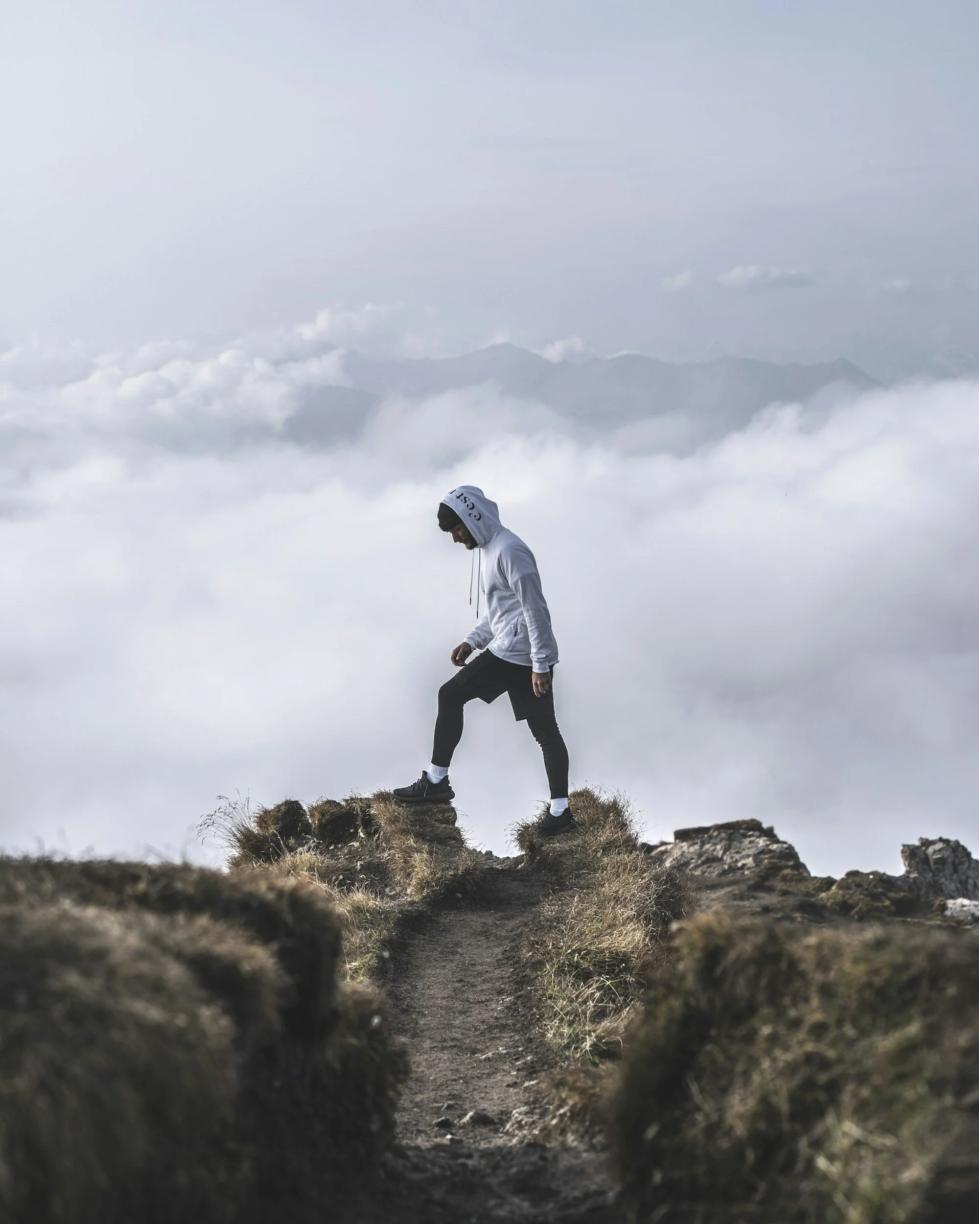 Hiker walking along a rocky ridge above clouds.