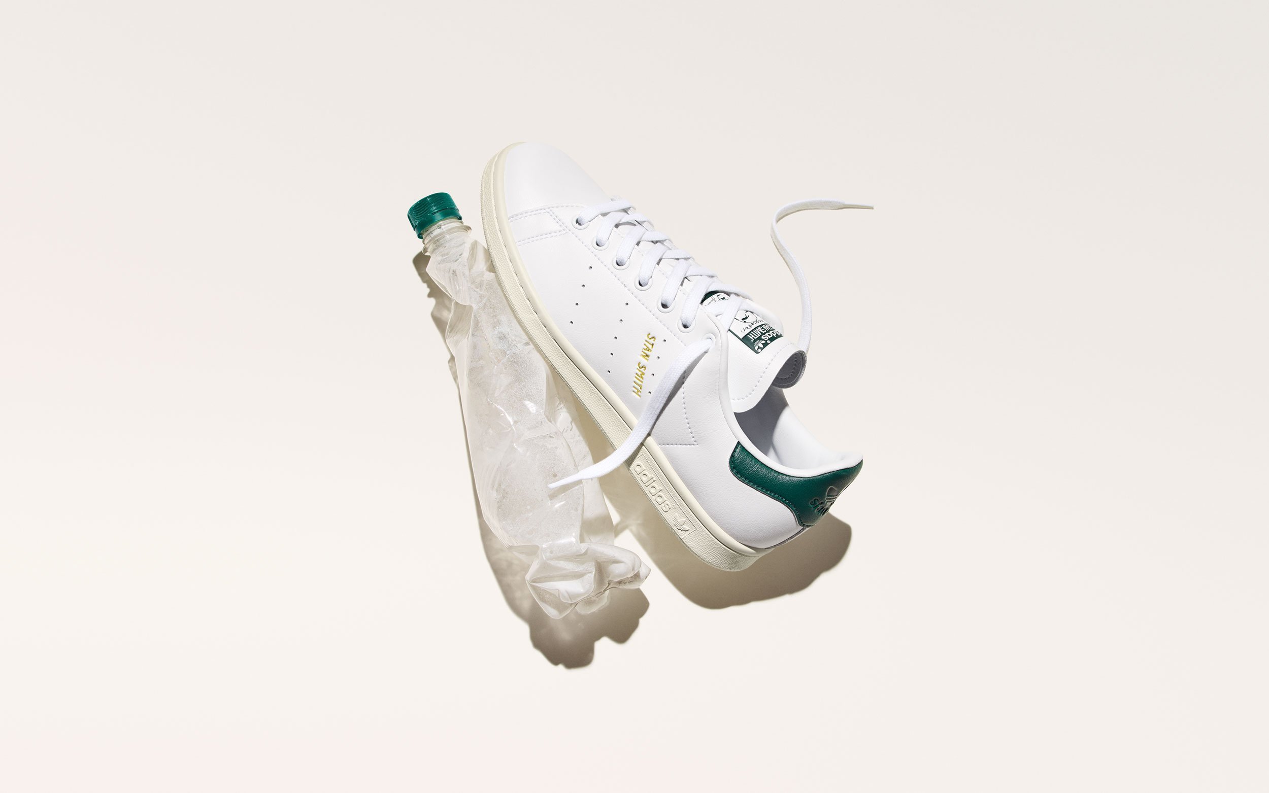 White sneaker with green accents, a green cap on the heel, and a plastic water bottle stuffed into the shoe's opening, placed on crumpled tissue paper against a plain white background.