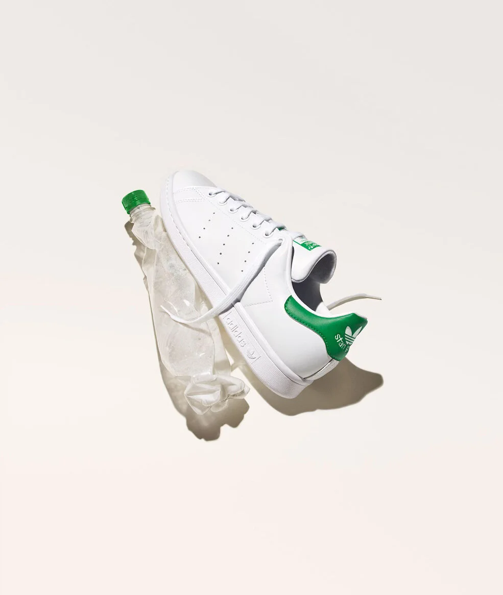 A white sneaker with green accents, a crumpled plastic water bottle, and a used plastic glove on a plain light background.