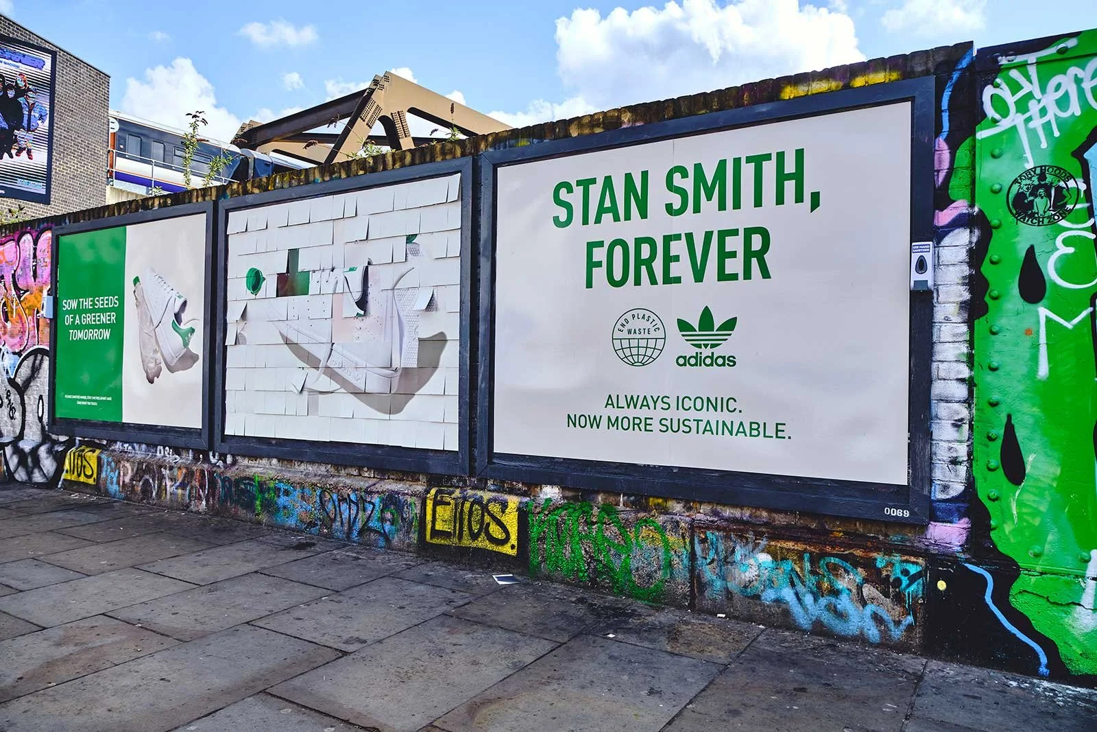 Graffiti-covered wall with advertisements for Adidas promoting sustainability and recycling, featuring green and white text that says "Stan Smith, Forever" and "Sow the Seeds of a Greener Tomorrow."
