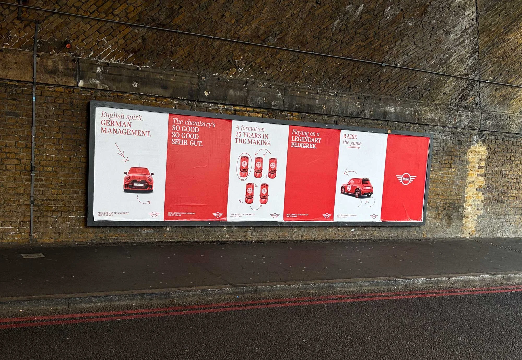 A large red poster advertising Mini car management, mounted on a brick wall in an underpass or tunnel, with a brick arched ceiling above.