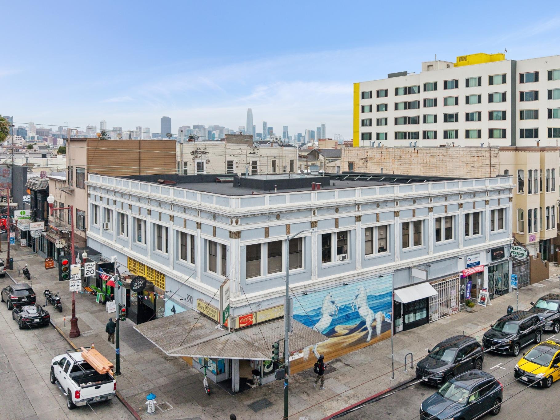City view showing a mix of historic and modern buildings, with a busy street below, cars parked along the curb, and pedestrians walking on the sidewalk.