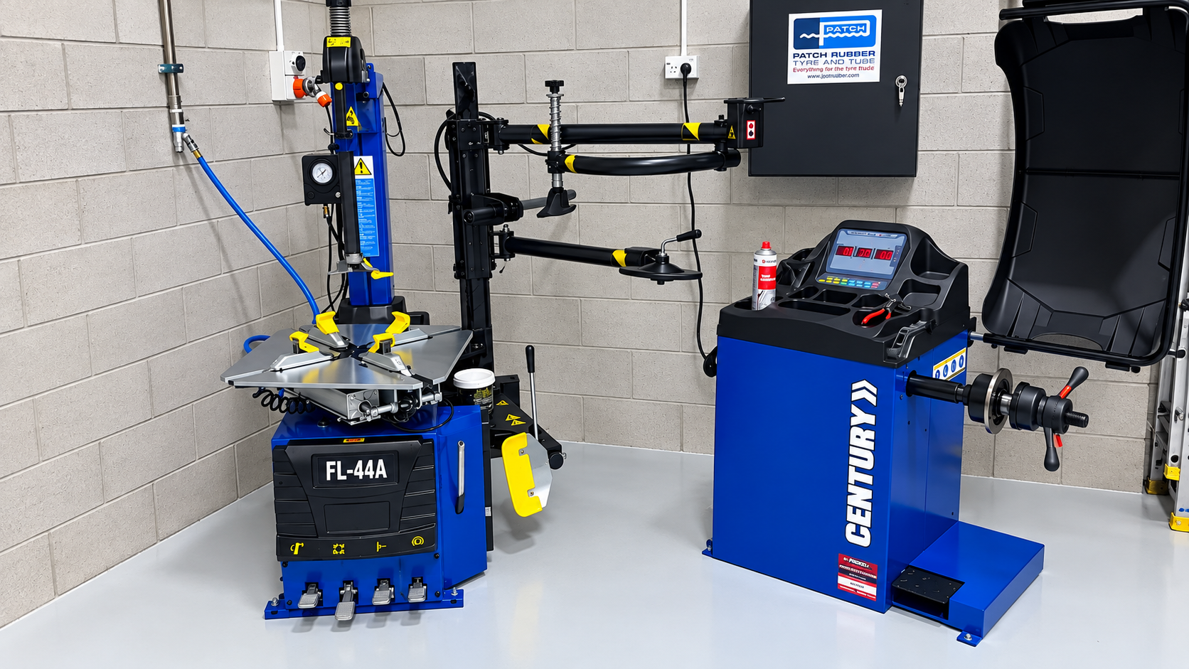 A tire mounting machine and an alignment machine in a workshop, with a brick wall and electrical panels in the background.