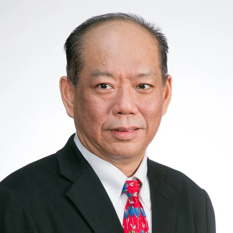 A middle-aged Asian man in a black suit, white shirt, and a colorful red and blue tie, posing against a plain white background.
