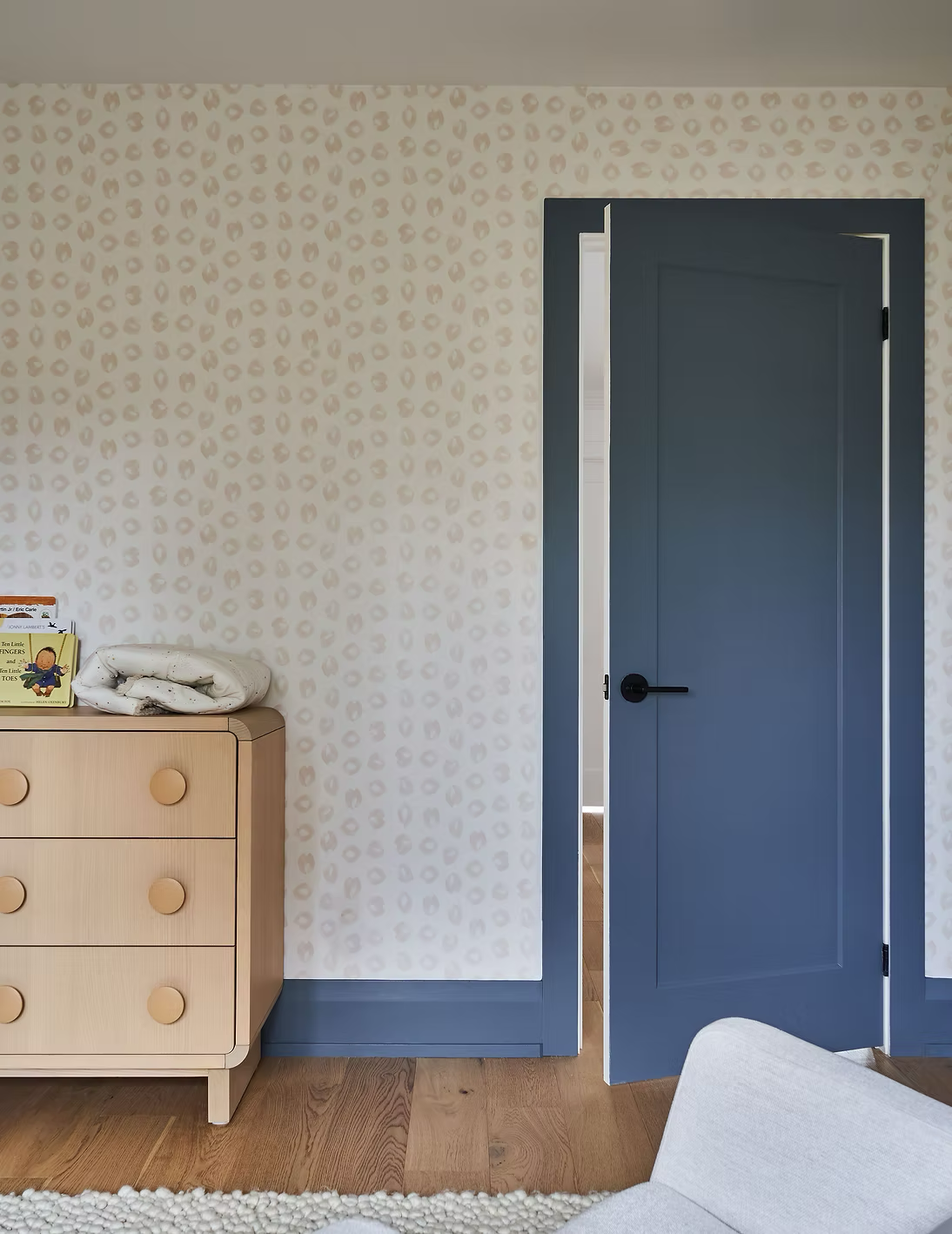 A bedroom corner with a light wood dresser, a blue door partially open, and a wall with beige and white leopard print wallpaper.