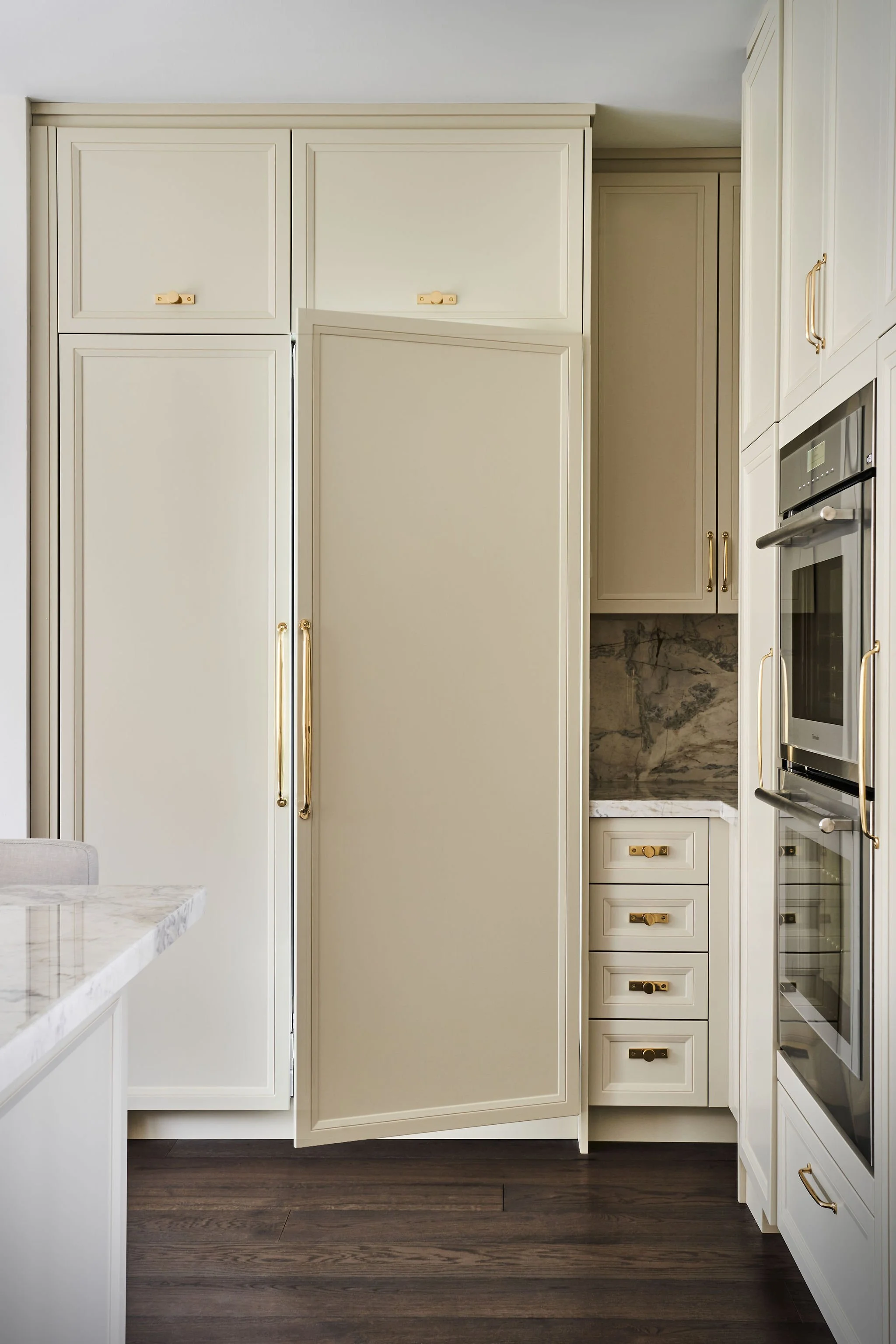 Kitchen with white cabinets, gold handles, a marble countertop, and dark hardwood flooring.