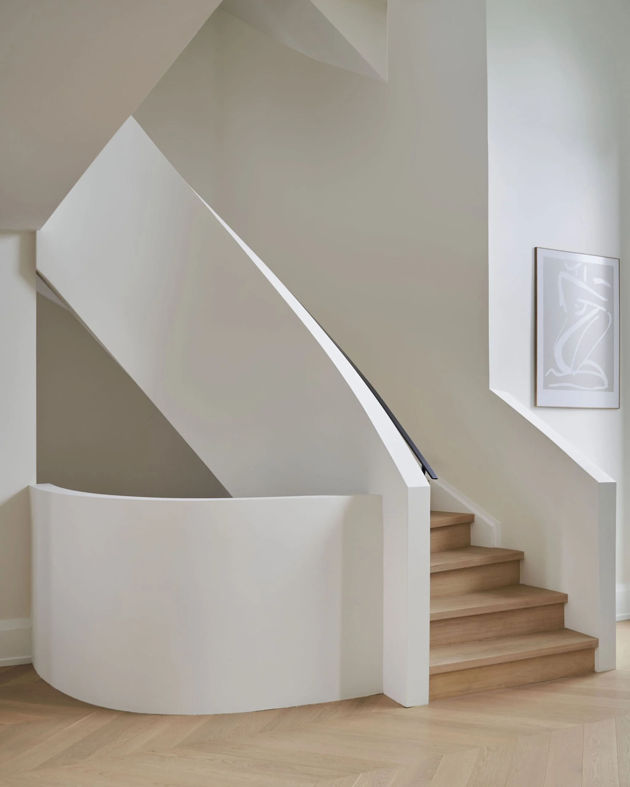 Modern interior staircase with wooden steps, white wall, partial view of framed art, and light wooden flooring.