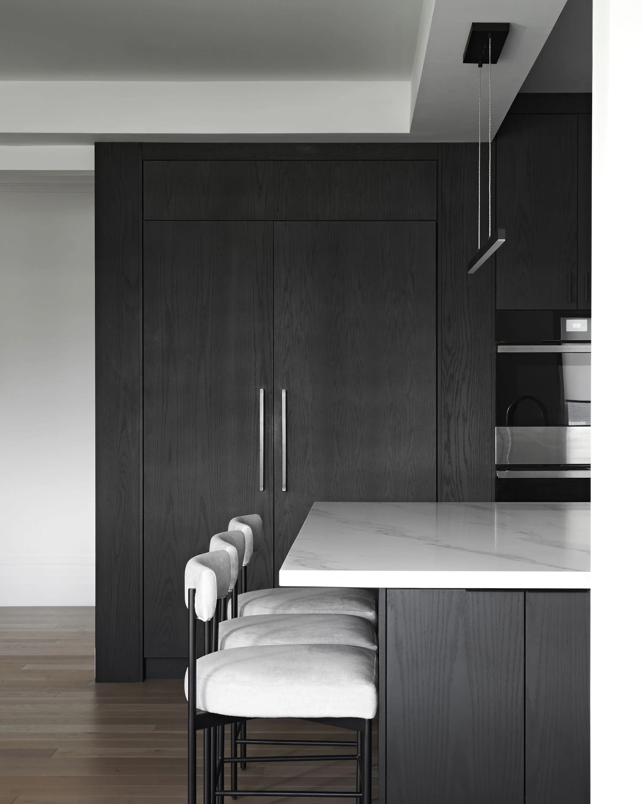 Modern kitchen with dark wood cabinets, a marble countertop, and white chairs with dark legs.