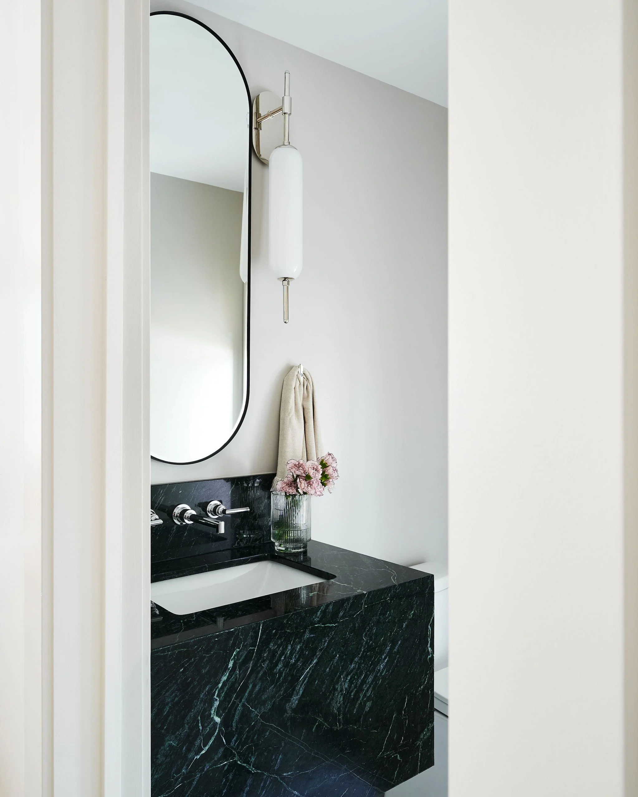 Bathroom mirror with black marble countertop, a small vase with pink flowers, and a towel hanging on the wall.
