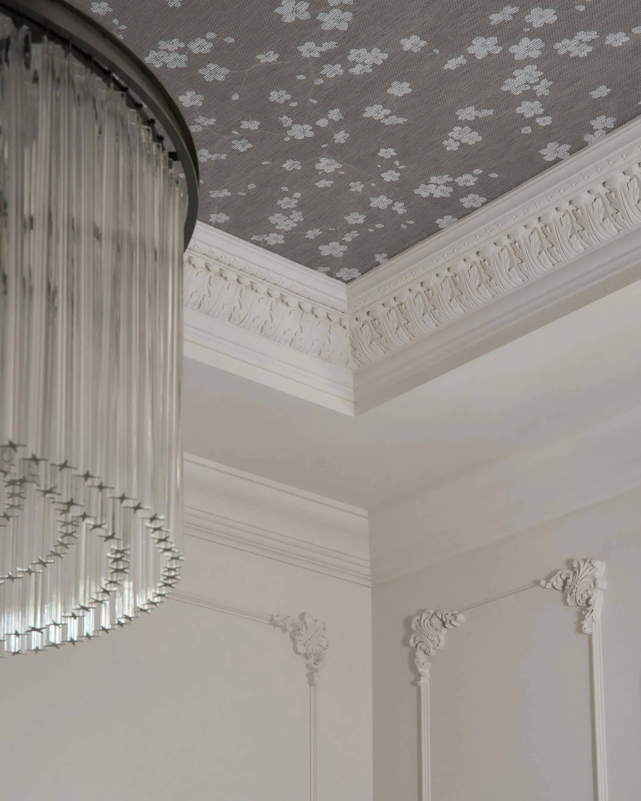 Ceiling with ornate crown molding, decorative appliqué, and a large circular chandelier with hanging crystal strands.