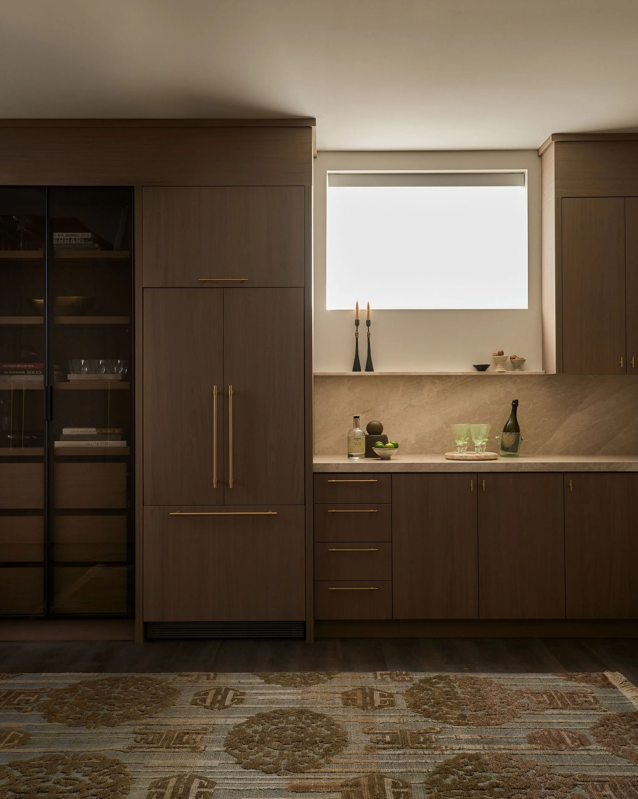 Modern kitchen with dark wood cabinets, a marble countertop, and decorative items including candles, bowls, and glasses, with a large window letting in natural light.