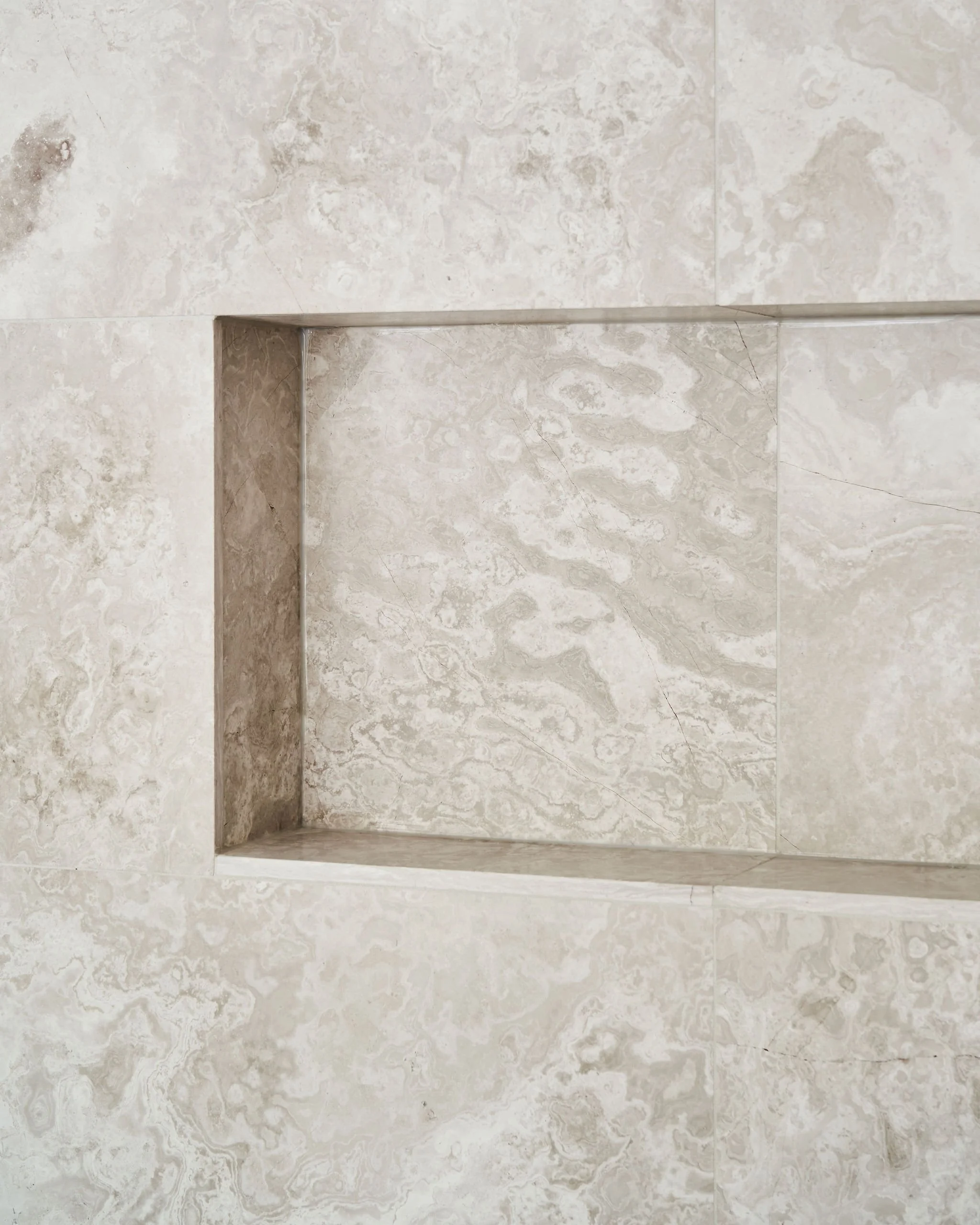Close-up of a built-in shower niche in a beige marble wall with subtle veining.