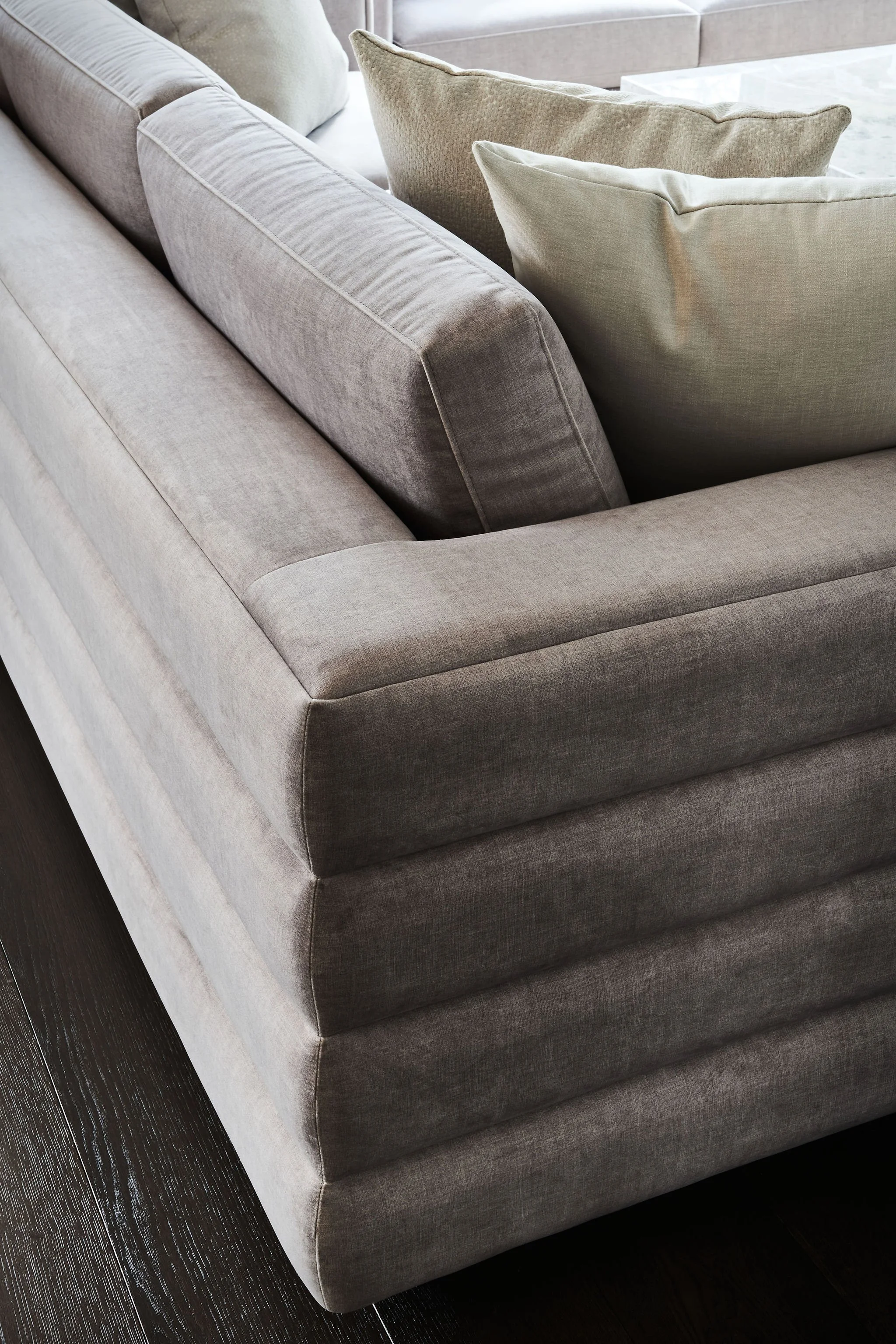Close-up of a beige fabric sofa with multiple cushions, on a dark wood floor.