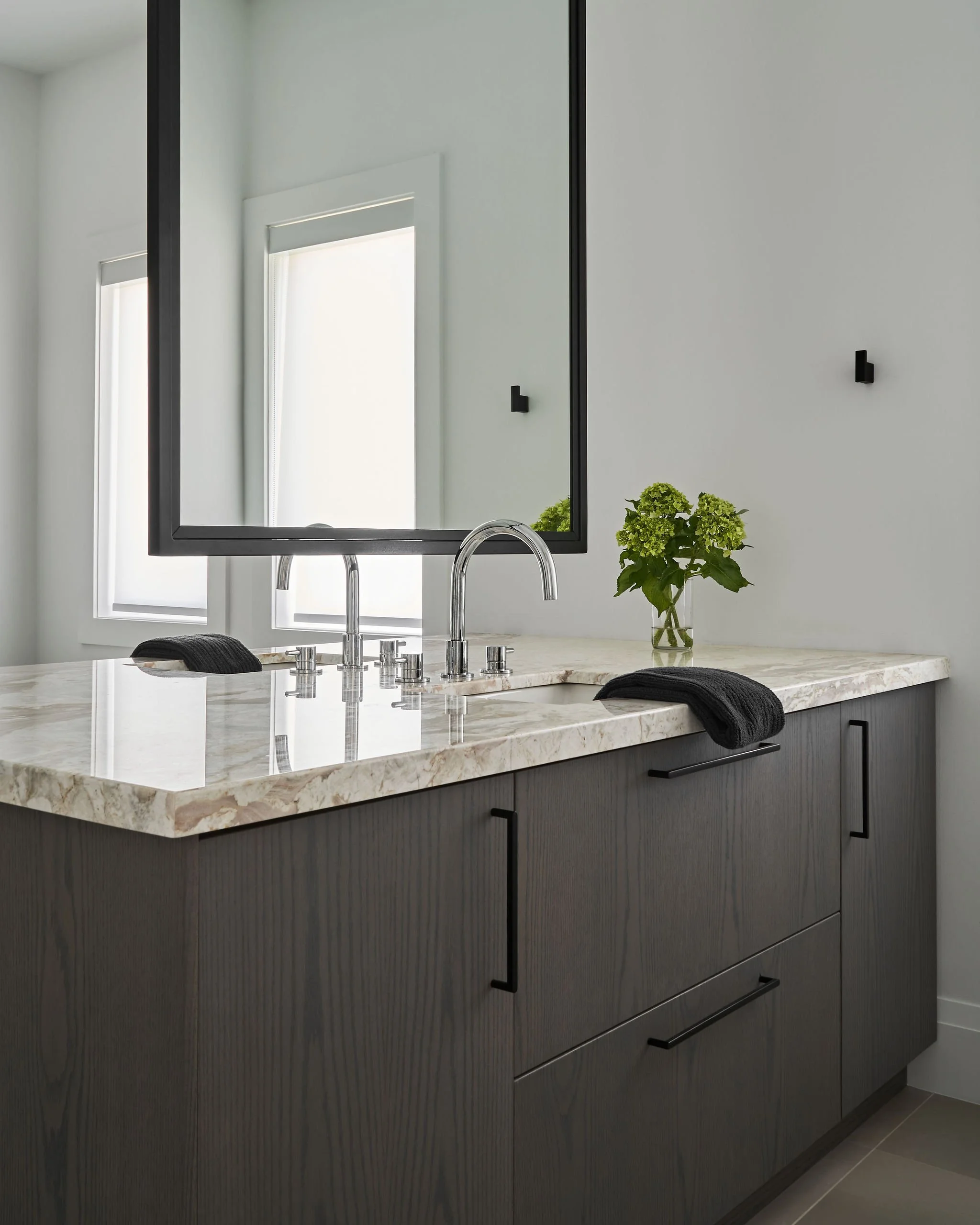 Modern bathroom vanity with a marble countertop, black cabinet with handle, a towel, a sink, a faucet, a mirror, a window, and a potted plant.