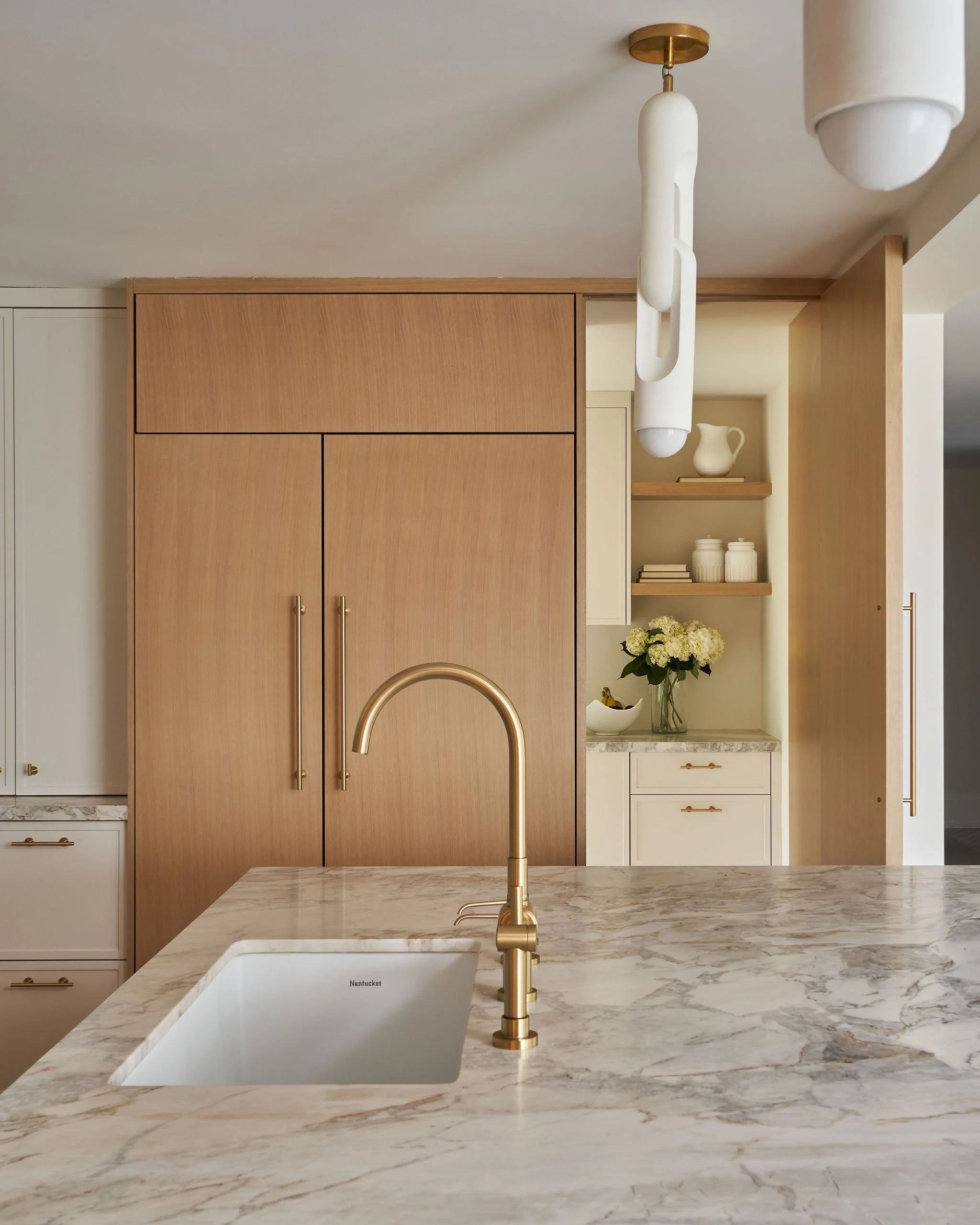 Modern kitchen with marble countertop, gold faucet, wooden cabinets, and open shelving with decorative items and flowers.