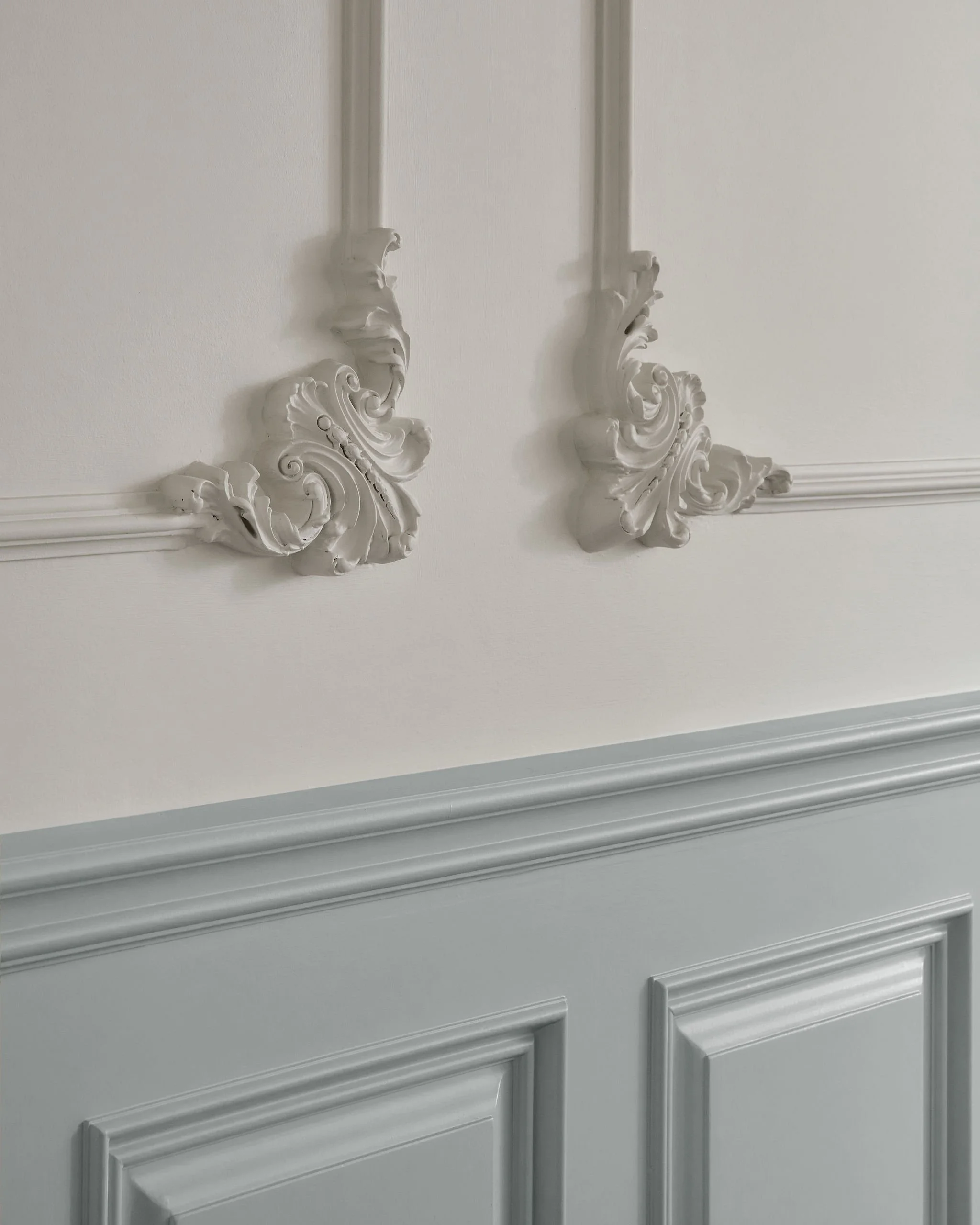 Close-up of a wall decorated with ornate white molding and wainscoting in a light gray room.