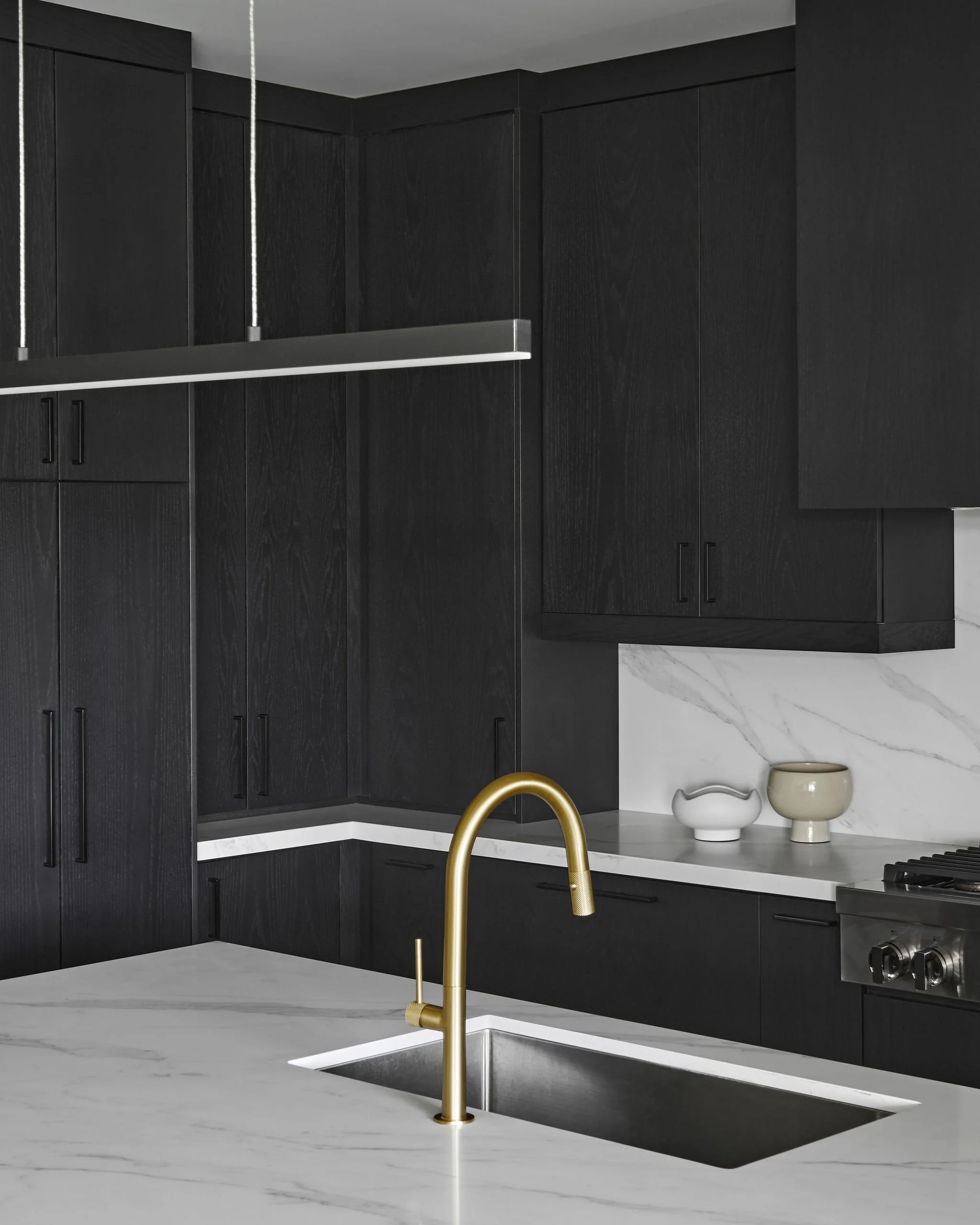 Modern kitchen with black cabinets, white marble countertops, gold faucet, and decorative vases on the counter.